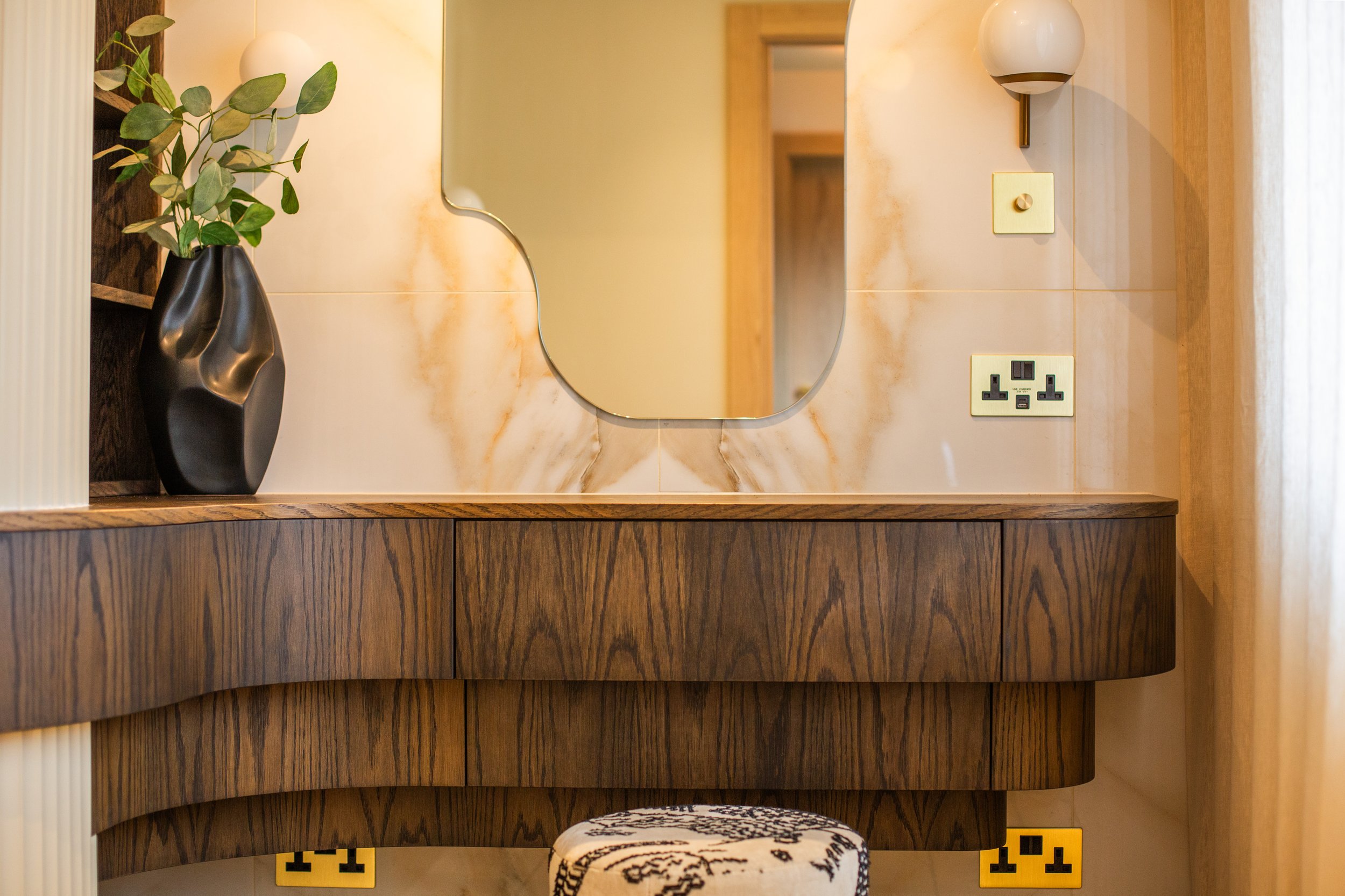 Bespoke curved dressing table in a small dressing room, featuring rich timber, a sculptural mirror, and integrated lighting — designed to follow the room’s architecture and maximise space.