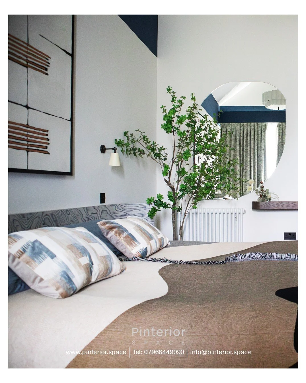 Bedroom view in a Cambridge Water Lane new‑build renovation, featuring a bespoke Elitis wallcovering artwork above a wood‑veneer headboard, layered neutral textiles, and a curved mirror reflecting soft natural light