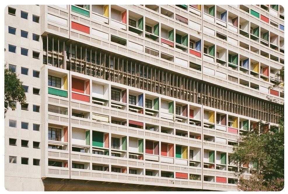 Modernist residential building facade with colourful panels, modular balconies, and vertical louvers in geometric rhythm.
