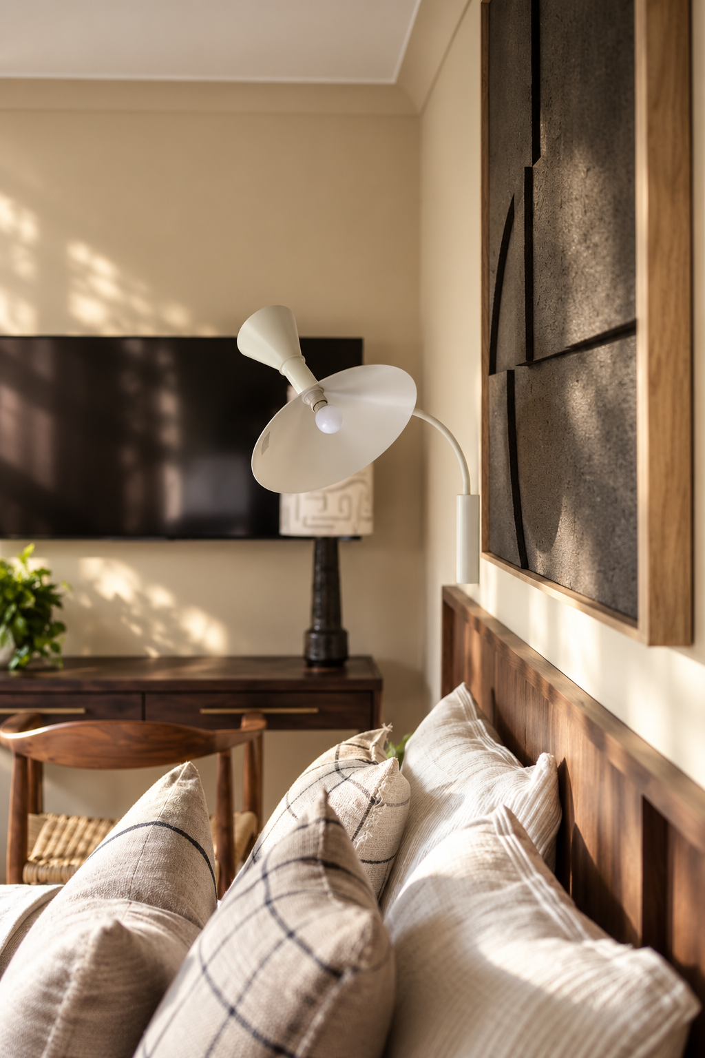 Warm contemporary bedroom detail in a Gamlingay renovation, with walnut joinery, layered cushions, sculptural lighting and soft natural shadows.