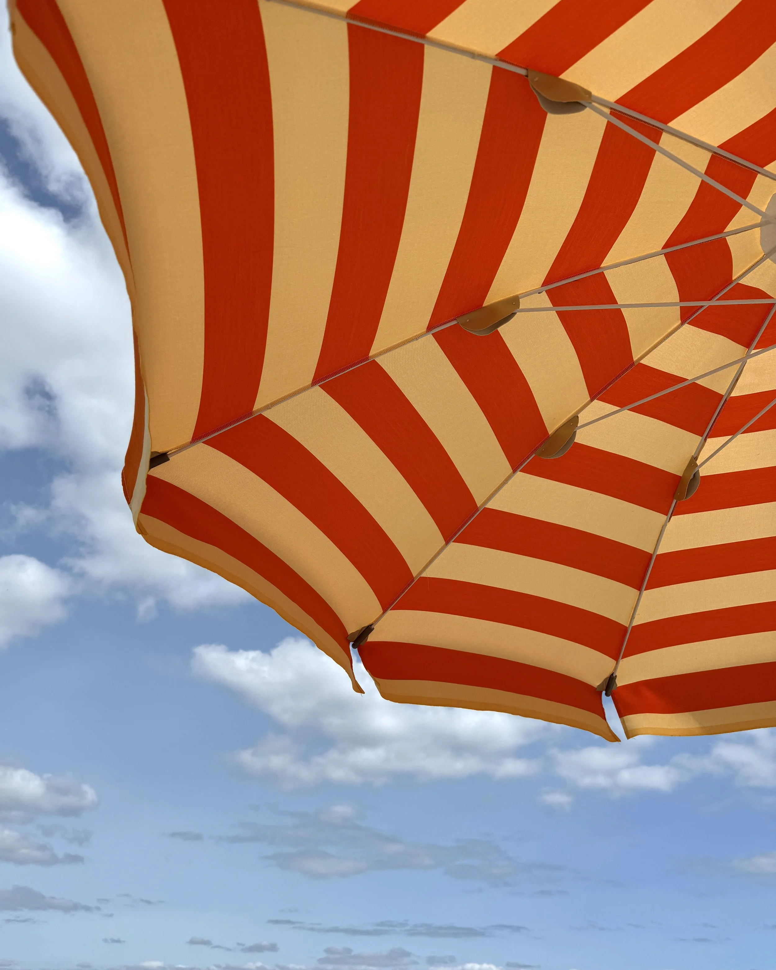 Orange og gulstribet parasol under blå himmel med skyer.