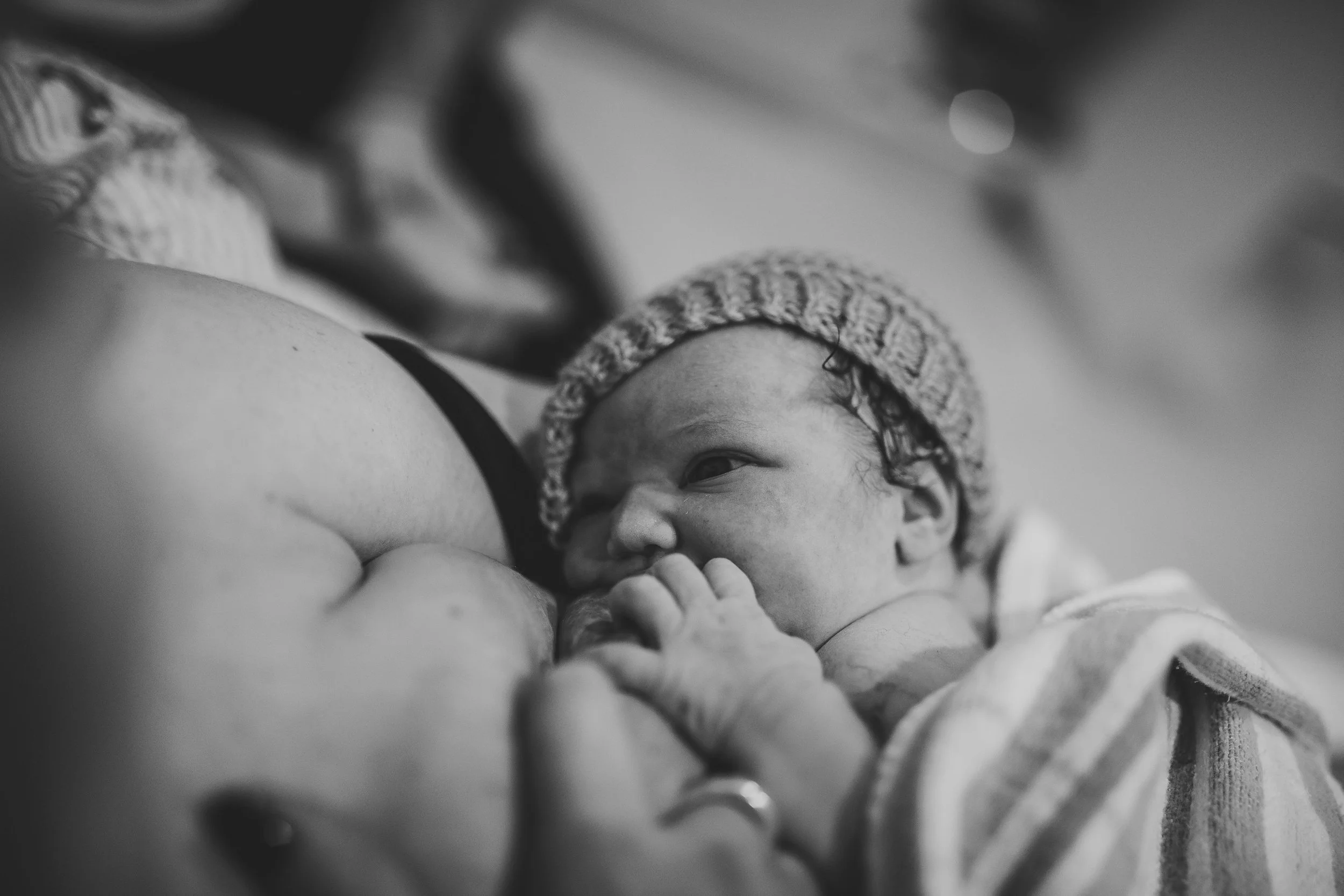 Newborn baby wearing a knit hat, being held close to a woman's chest, wrapped in a striped blanket. Black and white photo.