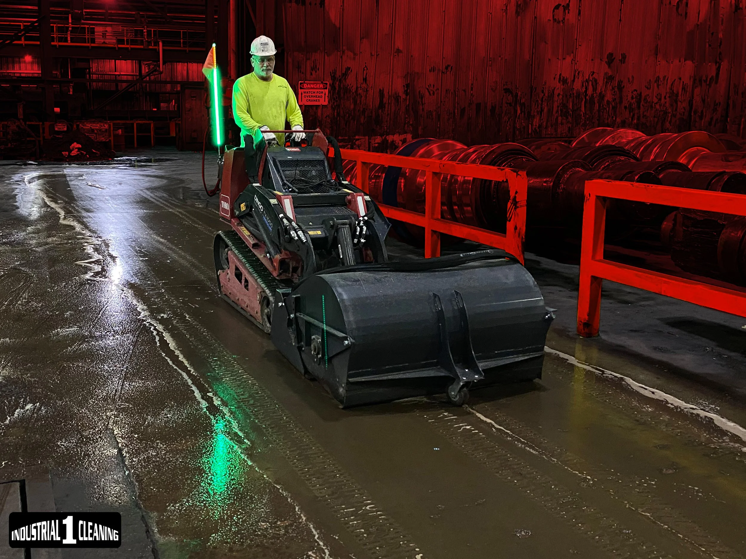 Worker operating a specialty ride-on floor scrubbing machine inside an industrial facility.