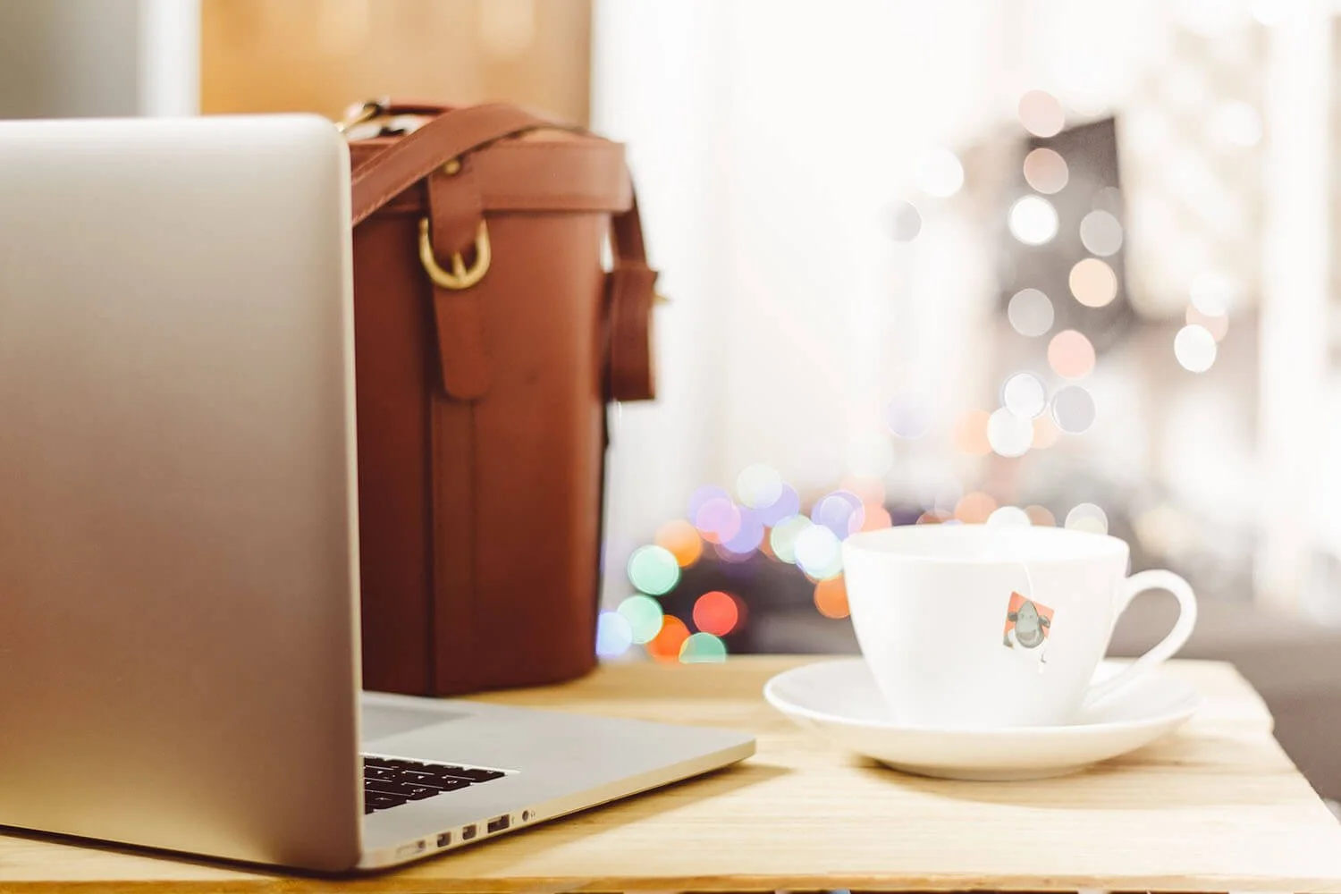 Table with some mottled lights behind it and a laptop, bag and teacup on it