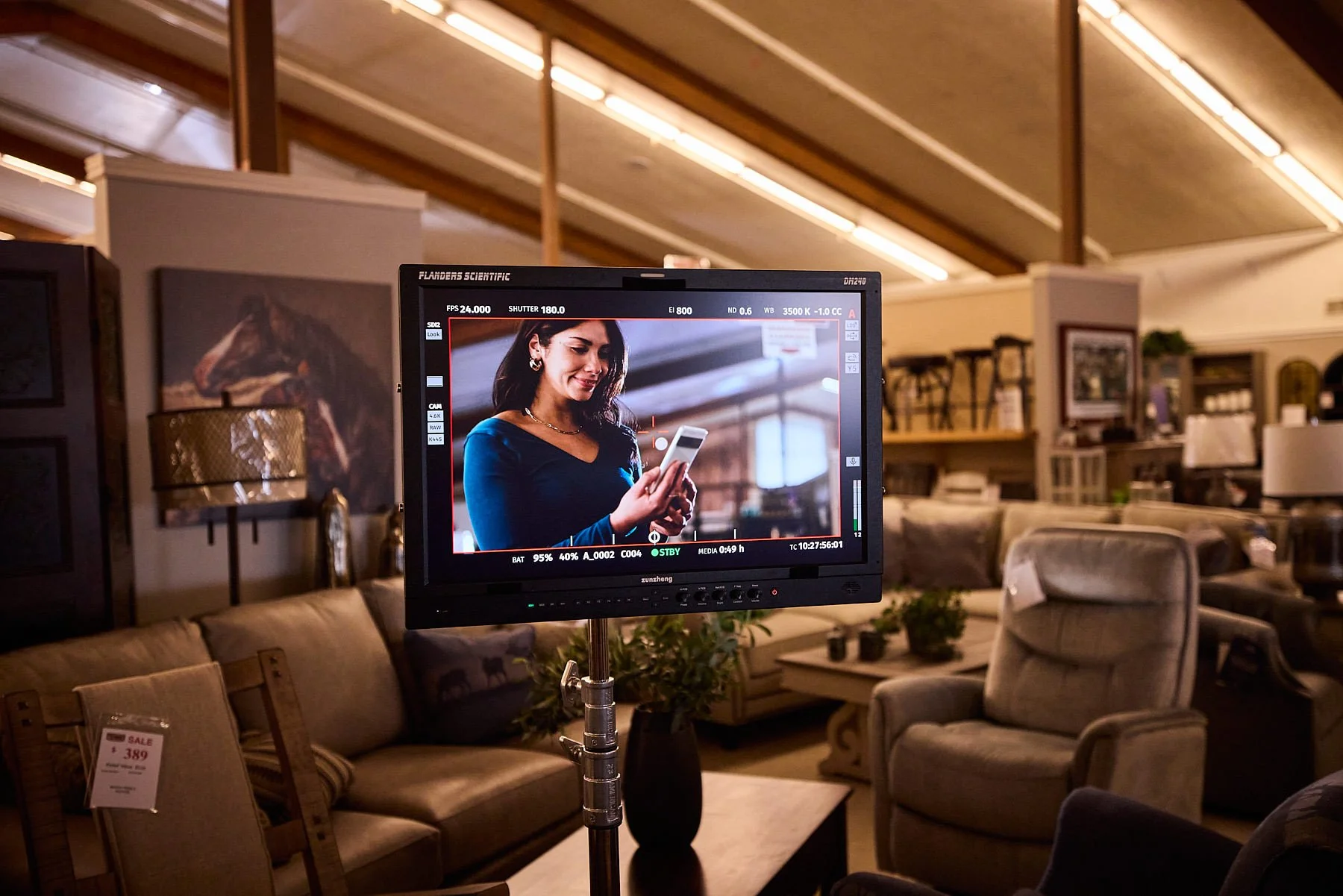 A television monitor displaying a scene of a woman in a furniture store looking at her phone, surrounded by various furniture items and decor.