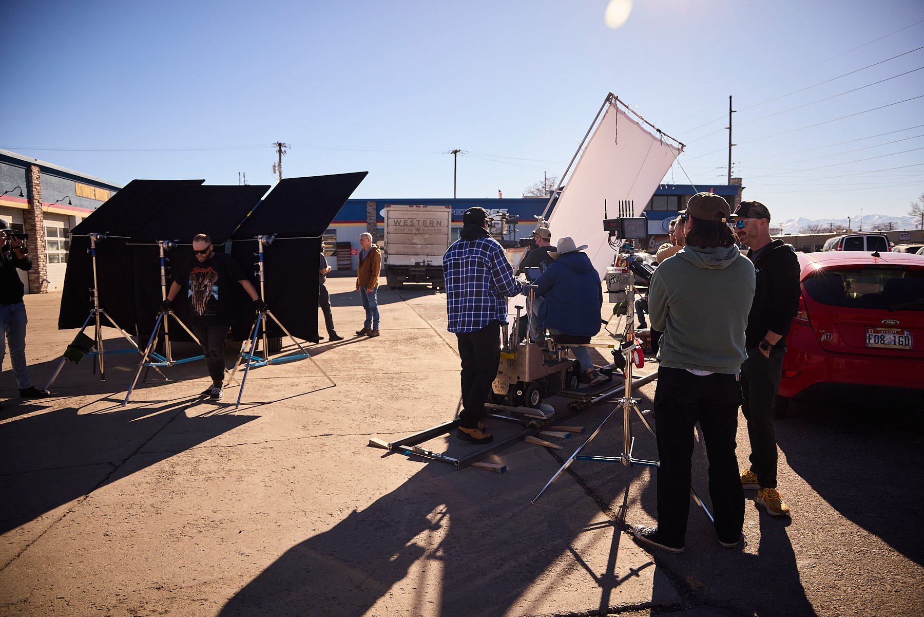 Film crew filming outdoors with camera, lighting, and equipment on a sunny day in a parking lot.