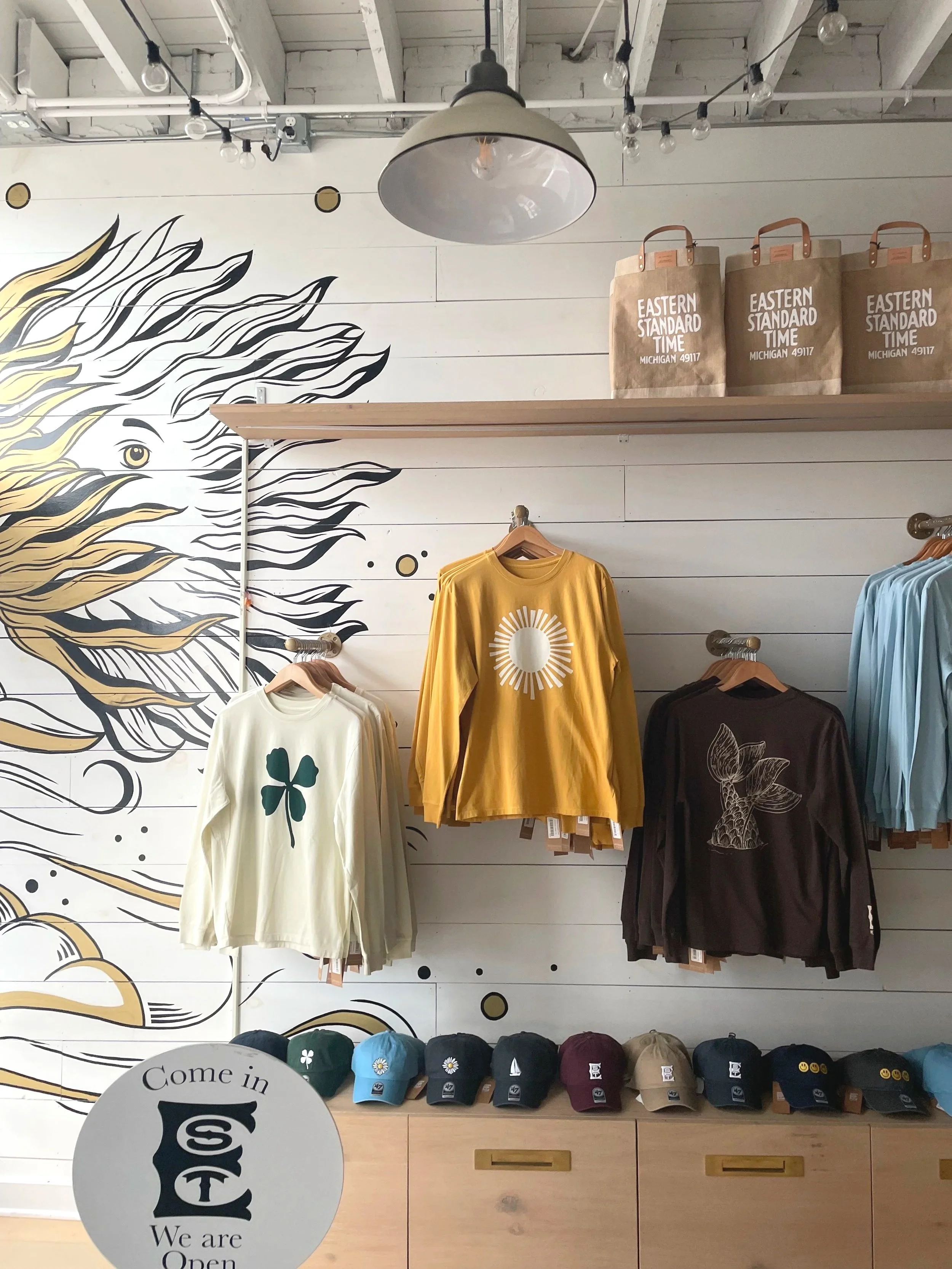 Display of t-shirts, hats, and bags in a store with a mural of a lion's face on the wall.