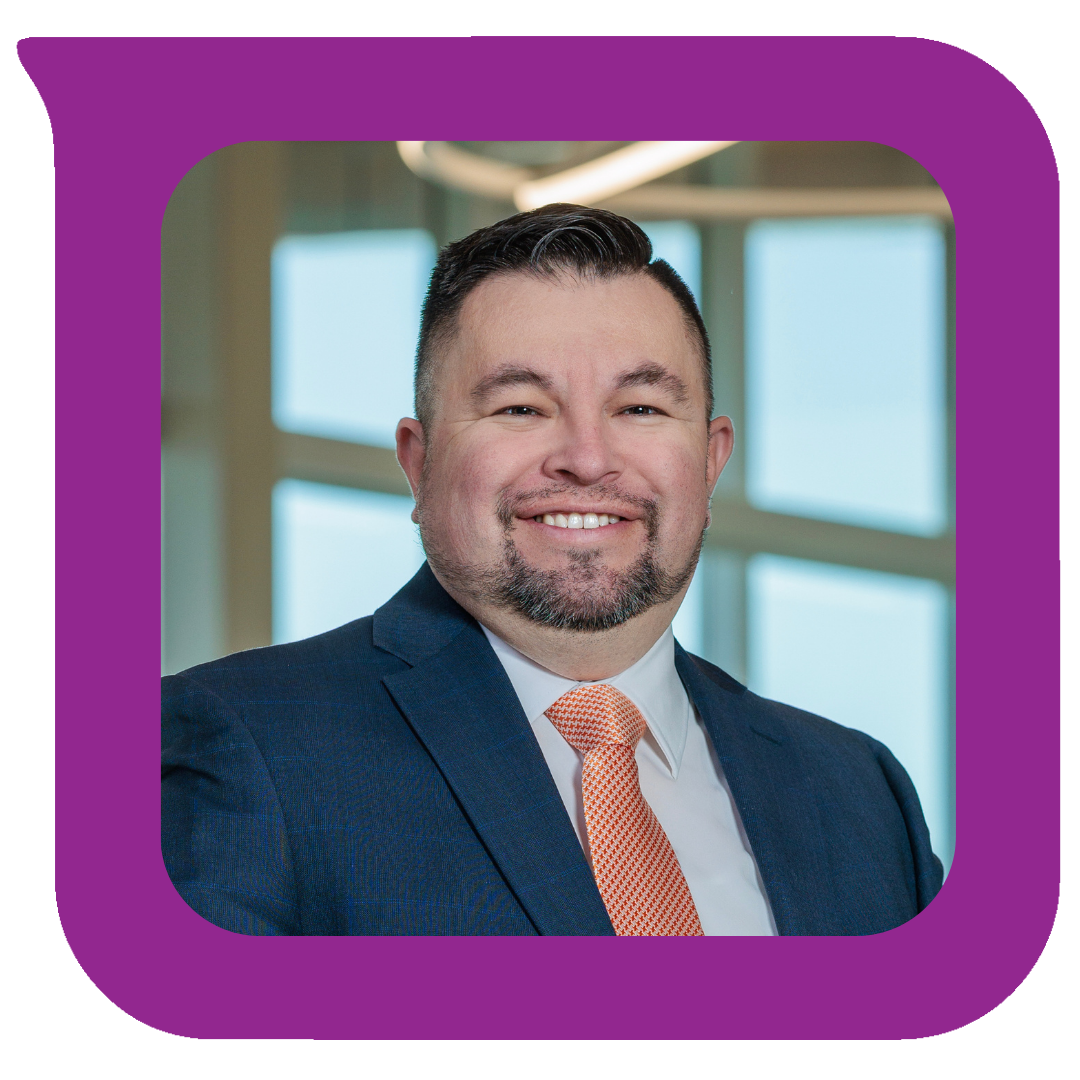 နောက်ခံတွင် ပြတင်းပေါက်ကြီးများဖြင့် ဝတ်စုံနှင့် တိုင်ဝတ်ဆင်ထားသော အမျိုးသားတစ်ဦး ပြုံးရွှင်နေပုံနှင့် ပရော်ဖက်ရှင်နယ်ဆန်ဆန် ရိုက်ကူးထားသော ဓာတ်ပုံ။