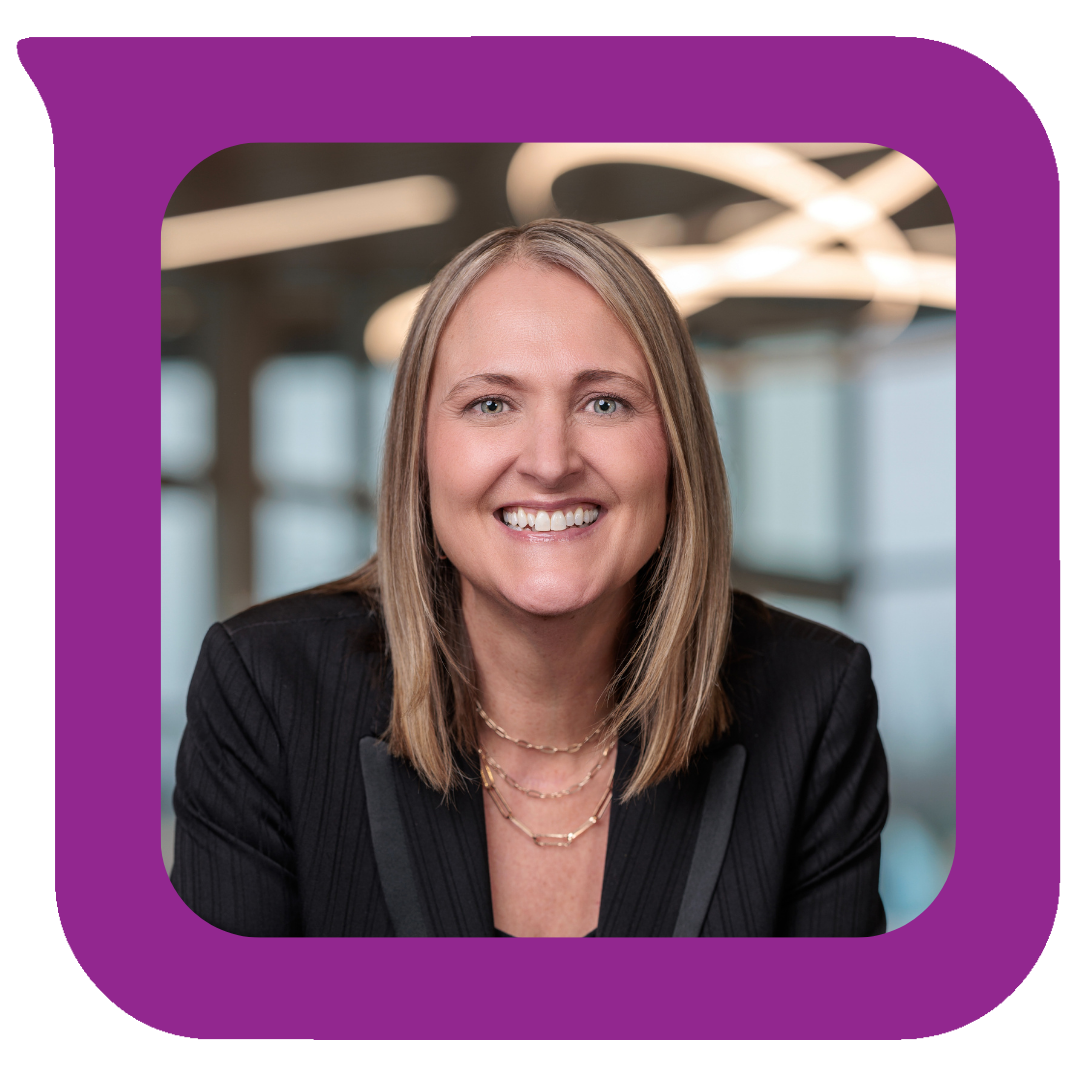 ရုံးခန်းထဲတွင် ပြုံးရွှင်နေသော အမျိုးသမီးတစ်ဦး၏ ပုံတူ၊ ပခုံးအထိရှည်သော ရွှေရောင်ဆံပင်၊ အပြာရောင်မျက်လုံးများ၊ အနက်ရောင်ဘလေဇာအင်္ကျီနှင့် အလွှာလိုက်ရွှေလည်ဆွဲများ ဝတ်ဆင်ထားသည့်ပုံ။