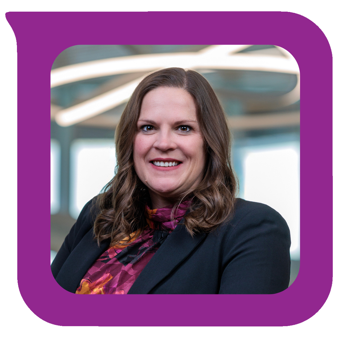 ပရော်ဖက်ရှင်နယ် အမျိုးသမီးတစ်ဦးသည် ပခုံးအထိရှည်သော အညိုရောင်ဆံပင်နှင့် အနက်ရောင် ဘလေဇာအင်္ကျီနှင့် ခရမ်းရောင်ပုံစံ ဘလောက်စ်အင်္ကျီကို ဝတ်ဆင်ထားပြီး ခေတ်မီရုံးခန်းတစ်ခုတွင် ပြုံးရွှင်နေသည်။