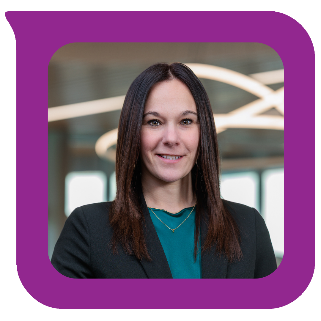 ပခုံးအထိရှည်သော အနက်ရောင်ဆံပင်၊ အနက်ရောင်ဘလေဇာနှင့် အပြာရောင်ဘလောက်စ်ကို ဝတ်ဆင်ထားသည့် ပရော်ဖက်ရှင်နယ်အမျိုးသမီးတစ်ဦးသည် ခေတ်မီမီးများနှင့် နောက်ခံတွင် ပြတင်းပေါက်များပါရှိသော ရုံးခန်းအတွင်း ပြုံးရွှင်နေသည်။