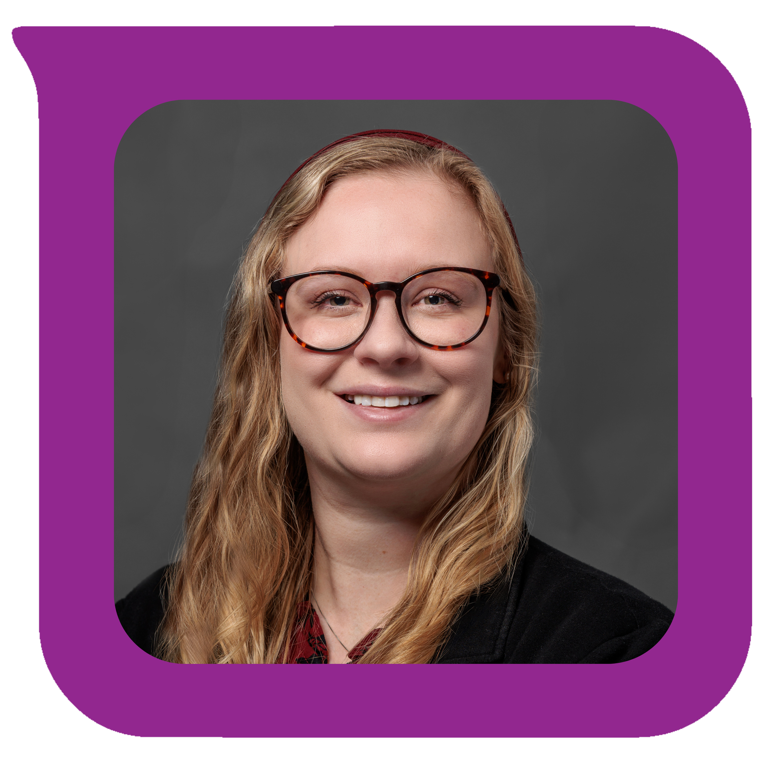 မီးခိုးရောင်နောက်ခံရှေ့တွင် ပြုံးရွှင်နေသော လိပ်ပြာခွံမျက်မှန်တပ်ထားသည့် လှိုင်းတွန့်ရွှေရောင်ဆံပင်ရှည်နှင့် အမျိုးသမီးတစ်ဦး။