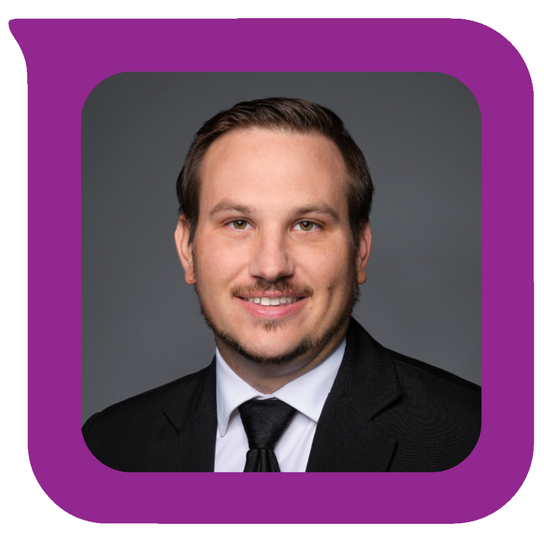 မီးခိုးရောင်နောက်ခံတွင် ပြုံးရွှင်နေသော ဆံပင်တိုအညိုရောင်နှင့် အနက်ရောင်ဝတ်စုံ၊ အဖြူရောင်ရှပ်အင်္ကျီနှင့် အနက်ရောင်နက်ကတိုင်ဝတ်ဆင်ထားသည့် လူငယ်တစ်ဦး၏ ခေါင်းရိုက်ဓာတ်ပုံ။