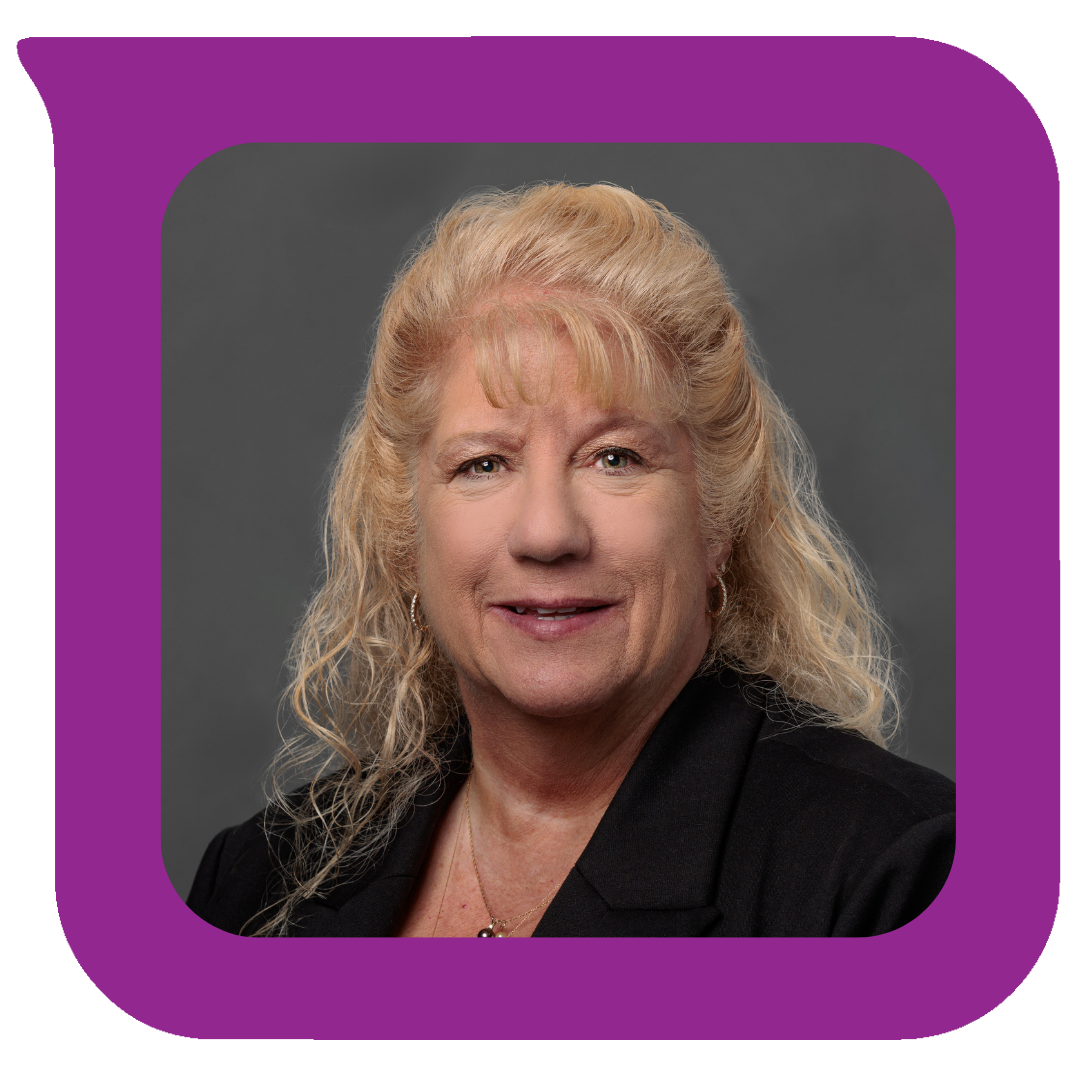 ရွှေရောင်ဆံပင်ကောက်ကောက်နဲ့ အသက်လတ်ပိုင်းအရွယ် အမျိုးသမီးတစ်ဦး၊ အနက်ရောင်ဘလေဇာအင်္ကျီနဲ့ ရွှေရောင်လည်ဆွဲကို ဝတ်ဆင်ထားပြီး မီးခိုးရောင်နောက်ခံမှာ ပြုံးနေပါတယ်။