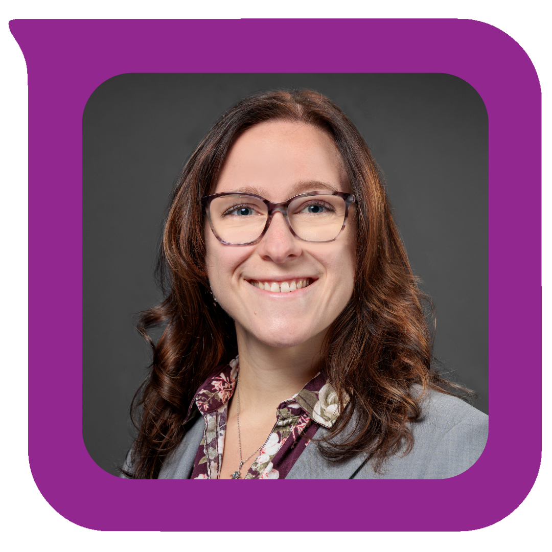 ပခုံးအထိရှည်သော အညိုရောင်ဆံပင်၊ မျက်မှန်တပ်ထားပြီး မီးခိုးရောင်ဘလေဇာအင်္ကျီနှင့် ပန်းပွင့်ရှပ်အင်္ကျီဝတ်ဆင်ထားသော အမျိုးသမီးတစ်ဦးသည် မီးခိုးရောင်နောက်ခံတွင် ပြုံးနေပုံ။