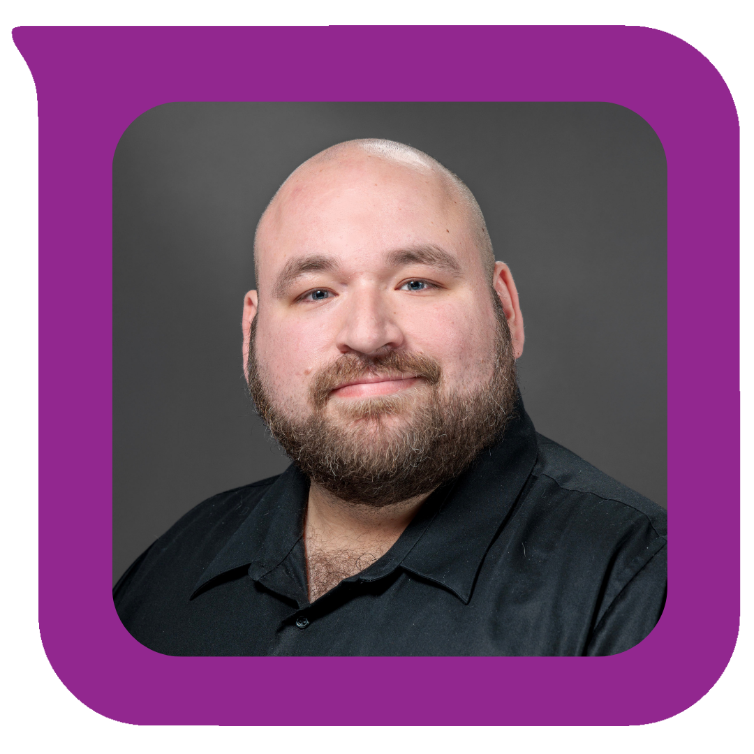 မုတ်ဆိတ်ရိတ်ထားပြီး ခေါင်းတုံးထားသော အမျိုးသားတစ်ဦးသည် မီးခိုးရောင်နောက်ခံတွင် ညင်သာစွာပြုံးနေပုံ။ ကော်လာအနက်ရောင်ရှပ်အင်္ကျီဝတ်ဆင်ထားသည်။