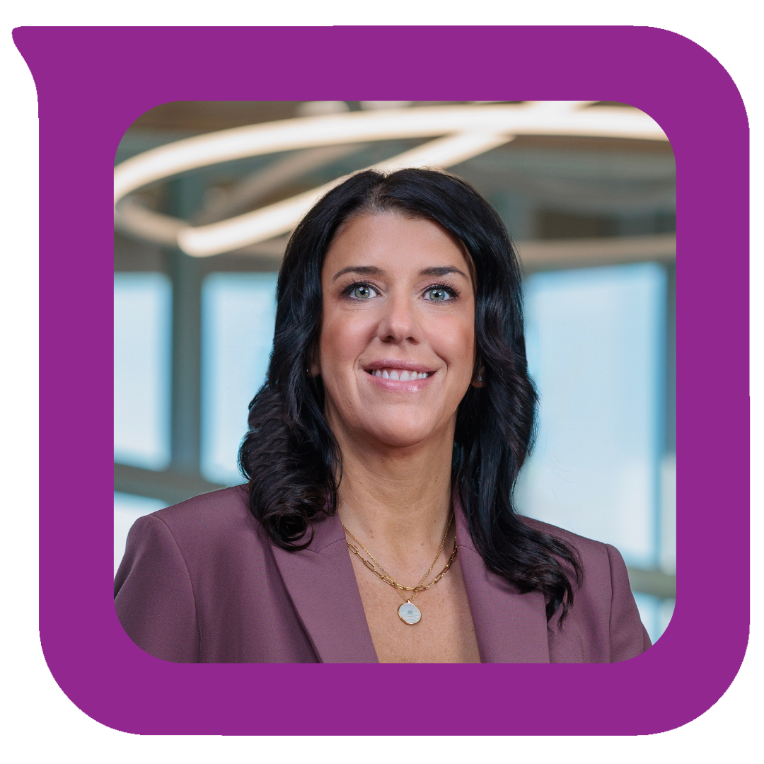 A woman with shoulder-length dark hair, blue eyes, and wearing a mauve blazer and gold jewelry, smiling in a professional setting.