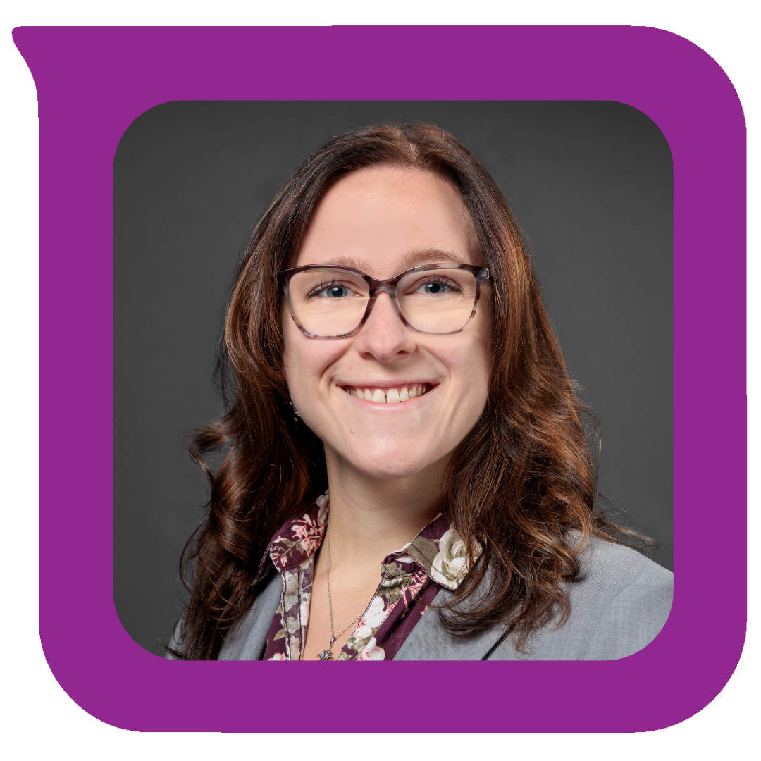 Headshot of a woman with shoulder-length brown hair, wearing glasses, a gray blazer, and a floral shirt, smiling against a dark gray background.