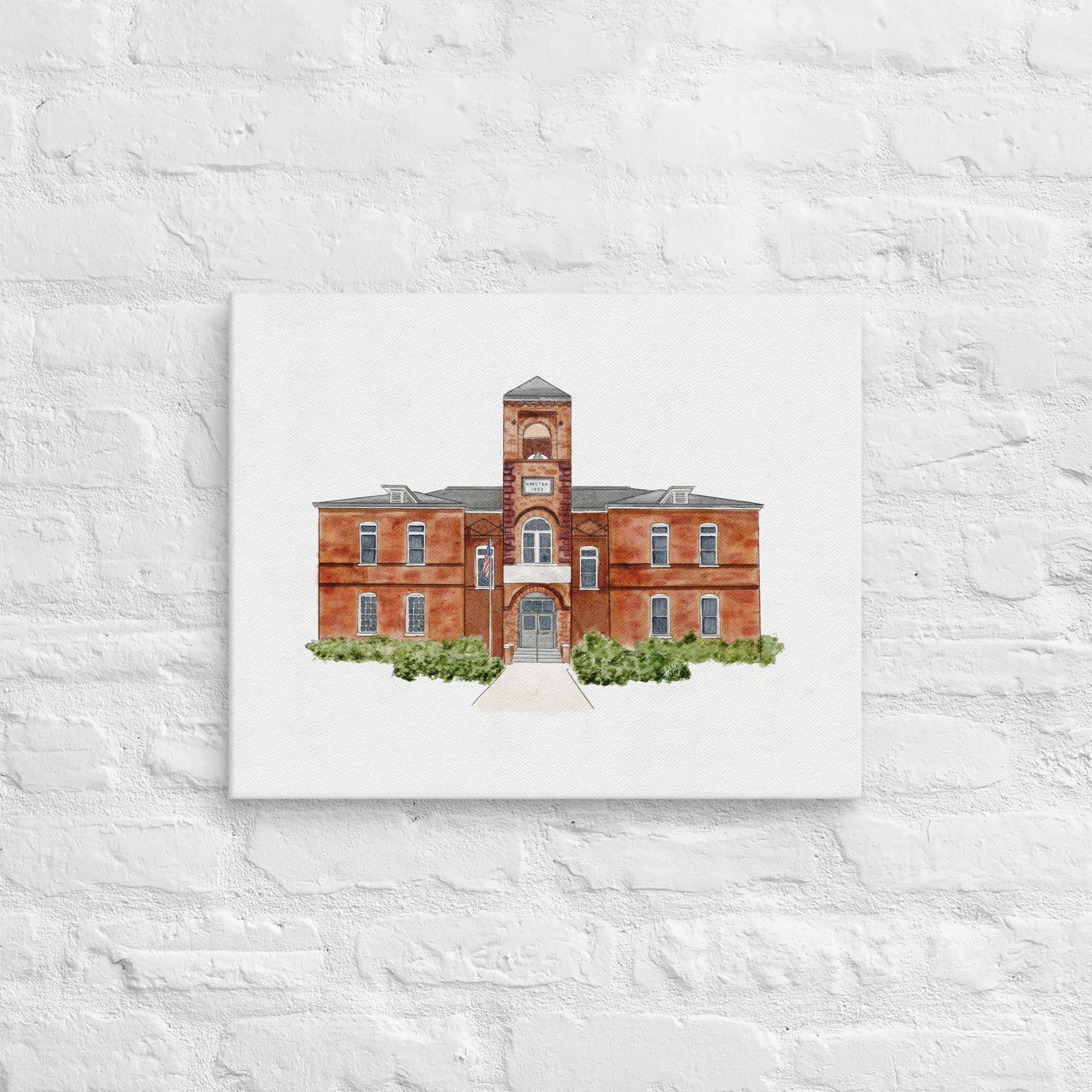 Watercolor painting of a historic brick building with a clock tower, American flags, and greenery in front, hung on a white brick wall.