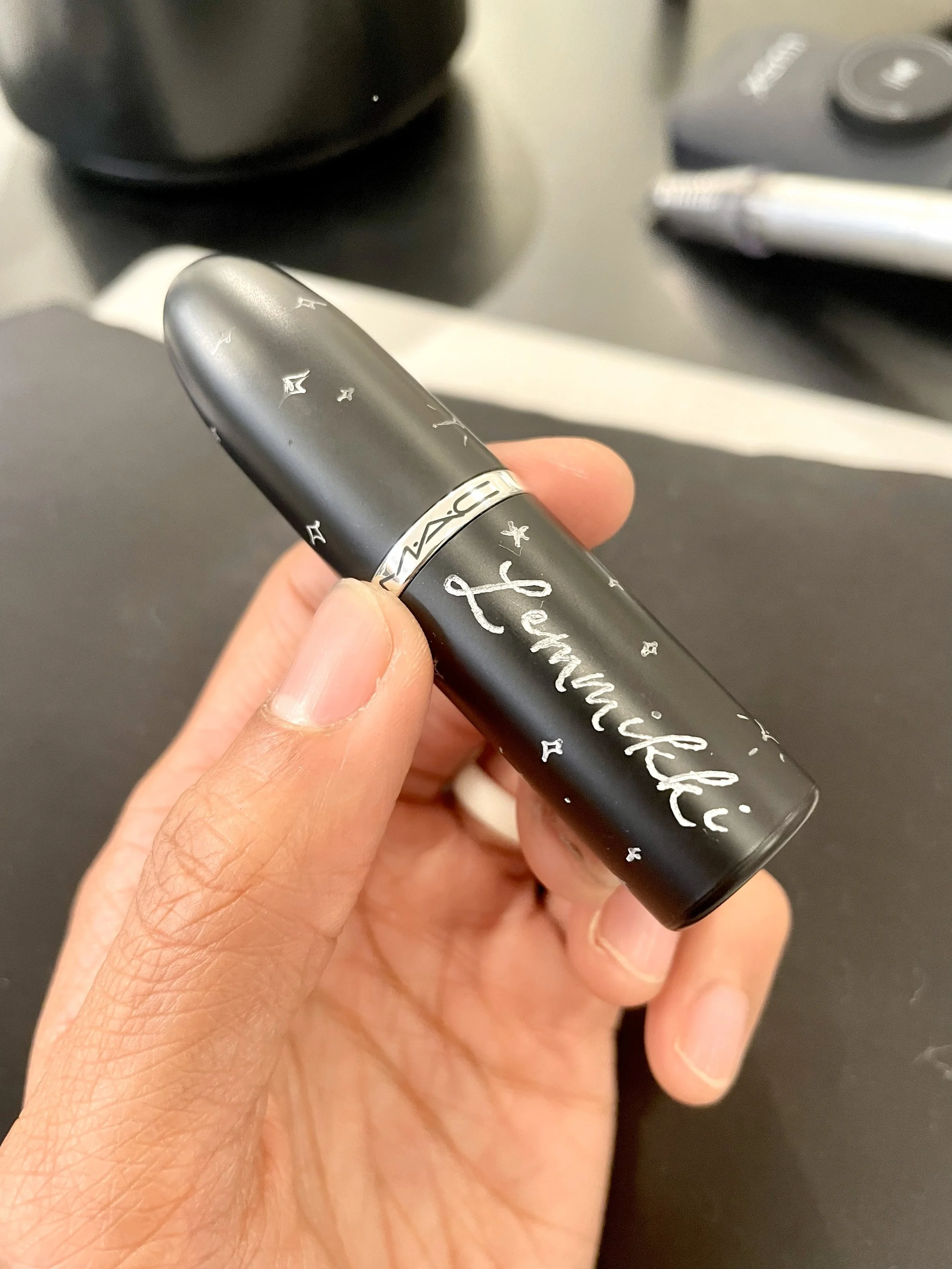  Hand holds a black MAC lipstick tube personalized with a name in white script—custom beauty item perfect for  live calligraphy and on-the-spot engraving  at an event.   