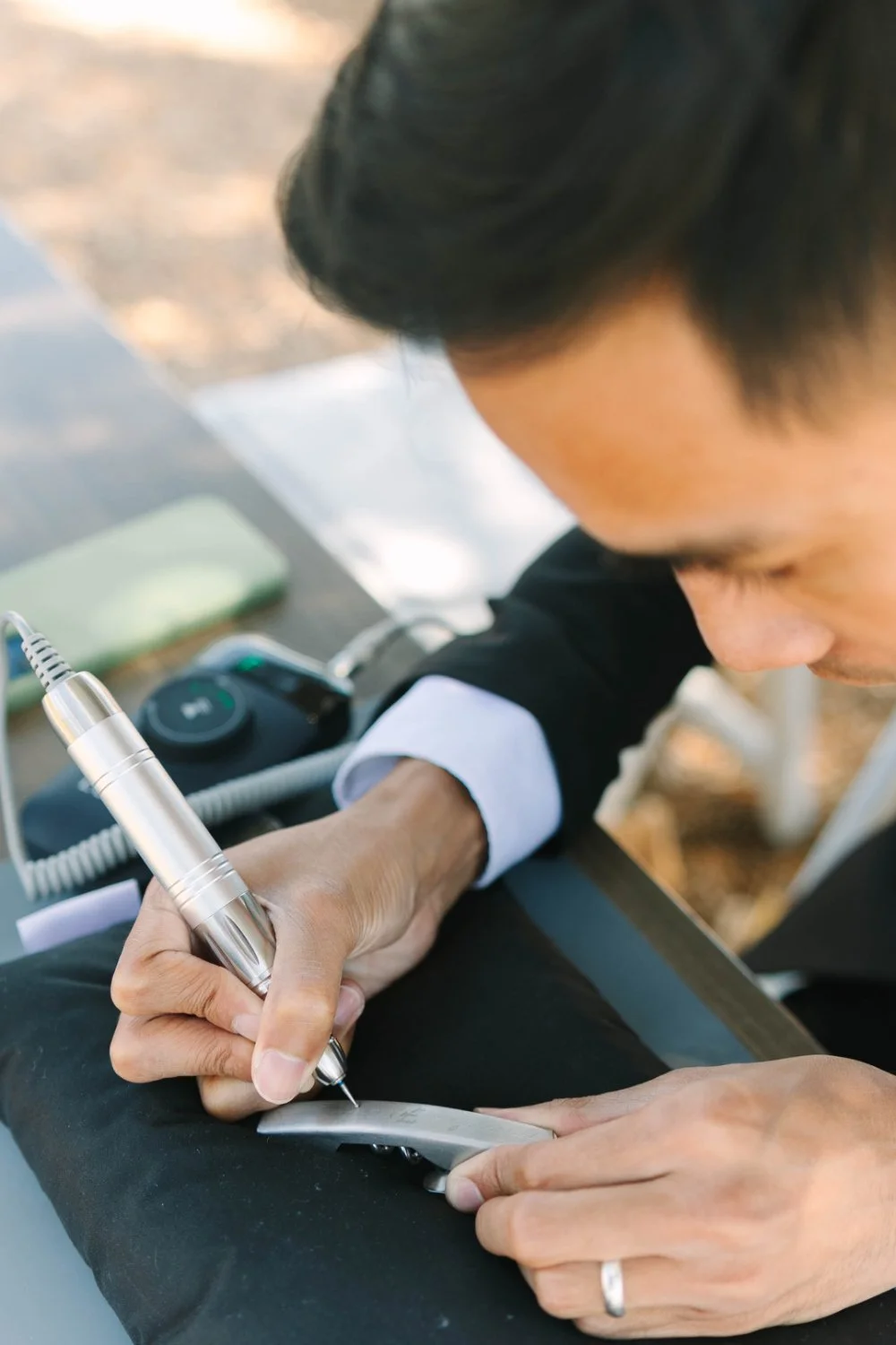 Close-up of an artist engraving a metal wine key outdoors with an electric tool—live calligraphy and on-the-spot engraving in action, showing careful detail work and personalization.