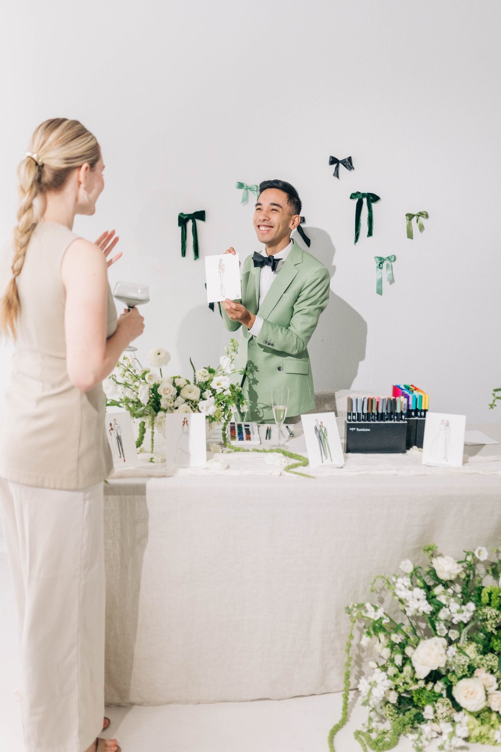 live wedding artist smiles as he hands a guest her finished portrait at a styled art table with florals and markers—an interactive wedding guest experience where guests feel seen, mingle naturally, and leave with a frame-worthy keepsake.