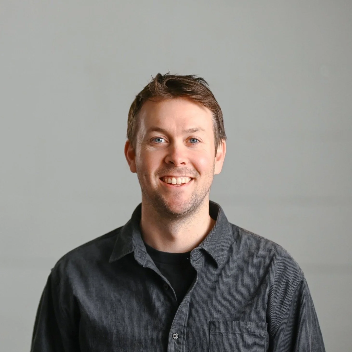 Smiling man with short brown hair standing against a light gray background