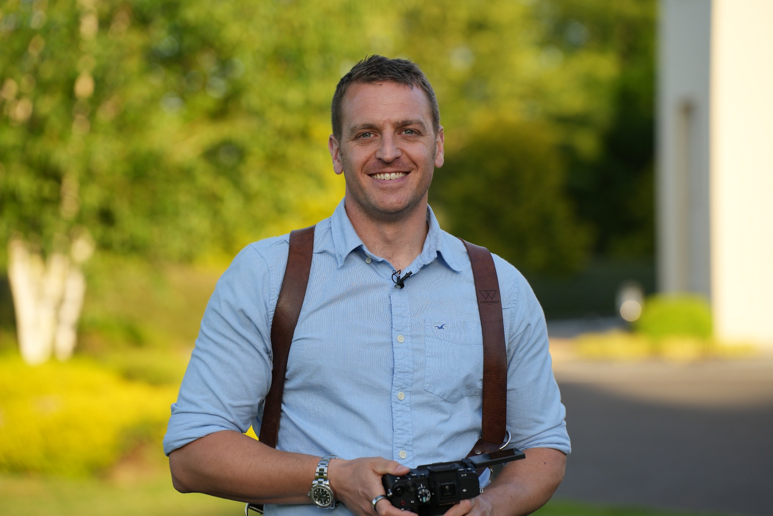 man with camera straps over his shoulders holding a DSLR camera in both hands