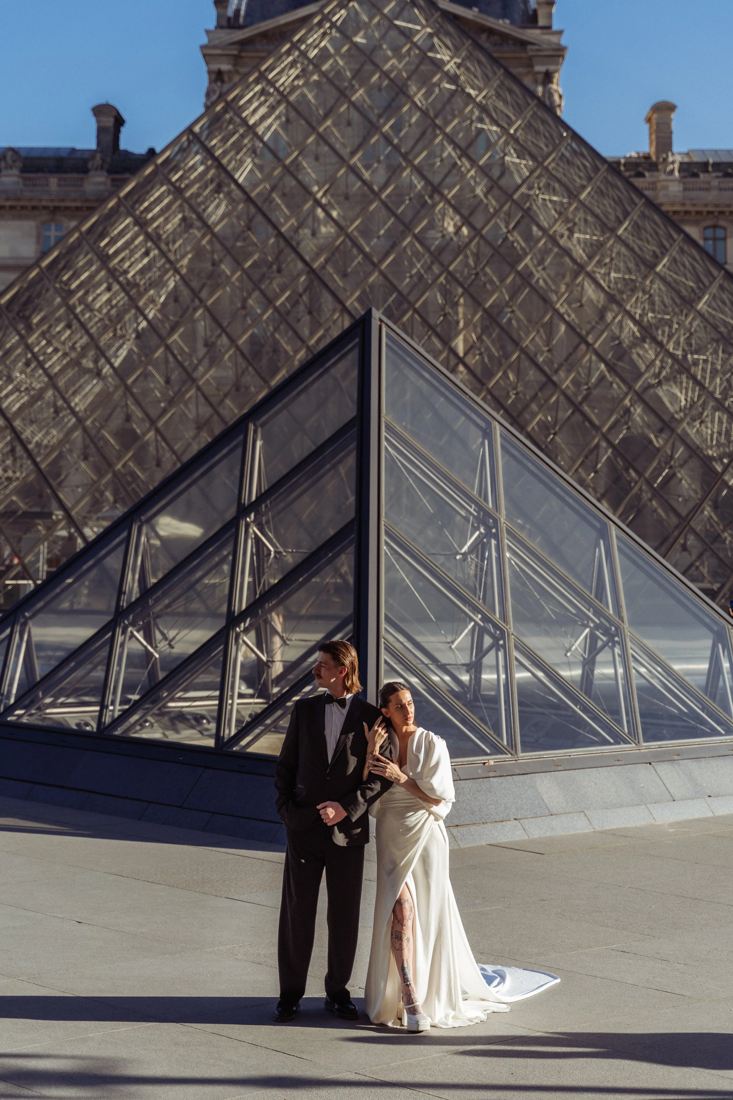 Couple standing outside the main louvre building - woman in a white dress and a man in a tuxedo