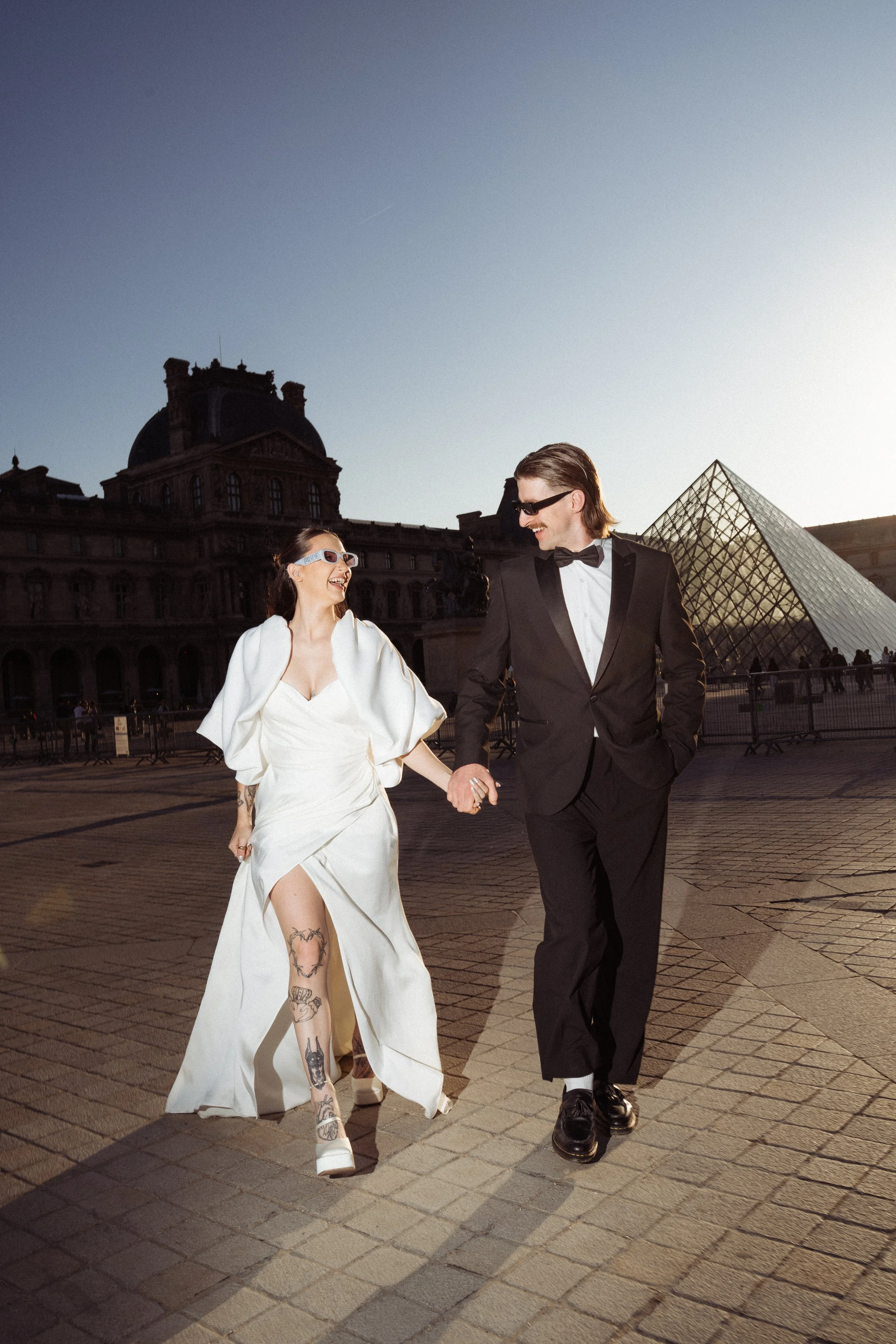 Couple walking towards the camera looking at each other with the louvre gallery in the background