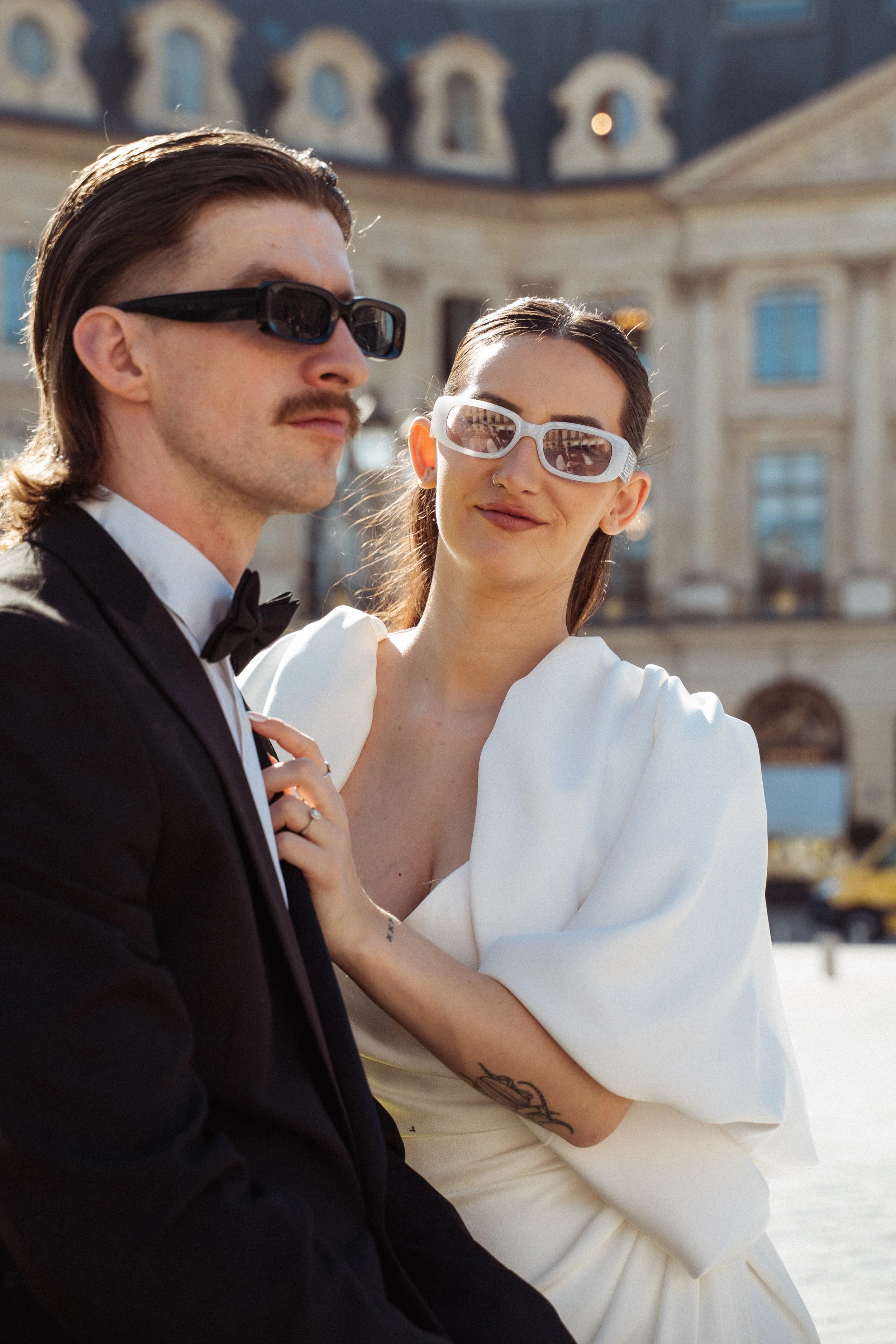 Woman looking at the camera whilst her husband looks off to the side with hotel ritz paris in the background