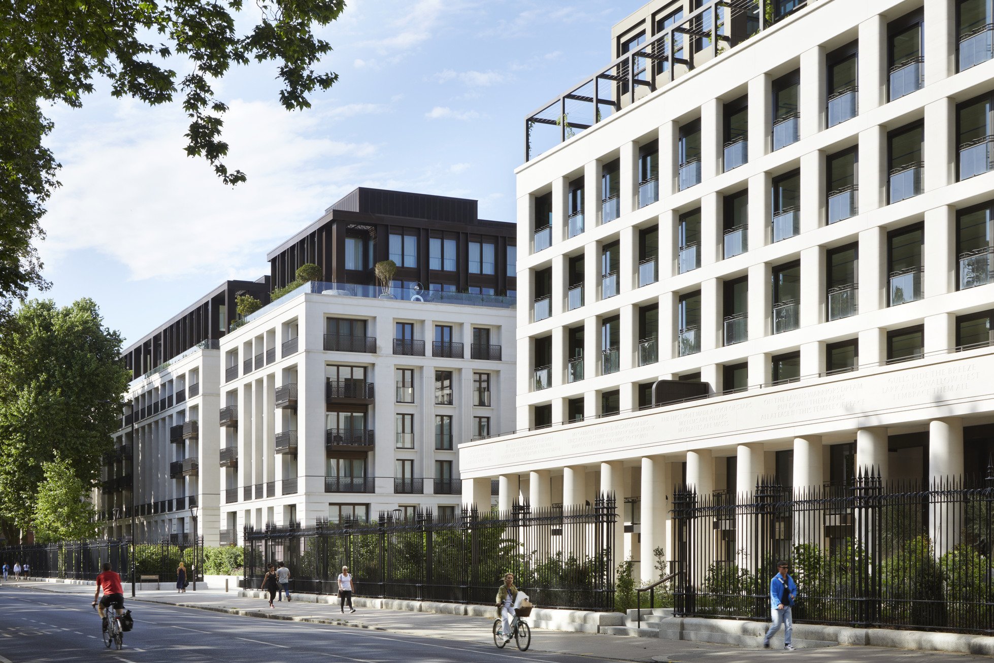 Chelase Barracks; a residential apartment building with multiple floors, balconies, and rooftop greenery, surrounded by a grassy lawn and trees under a clear blue sky.