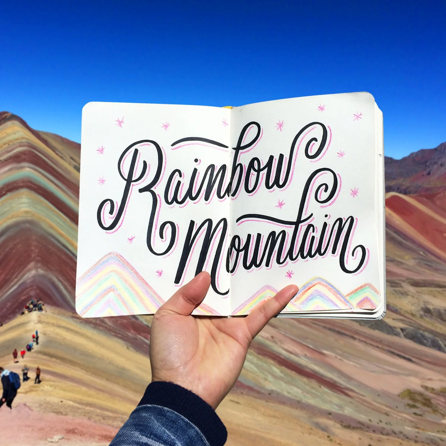 Sketchbook spread reading "Rainbow Mountain" surrounded by illustrated stars and rainbow mountain peaks.