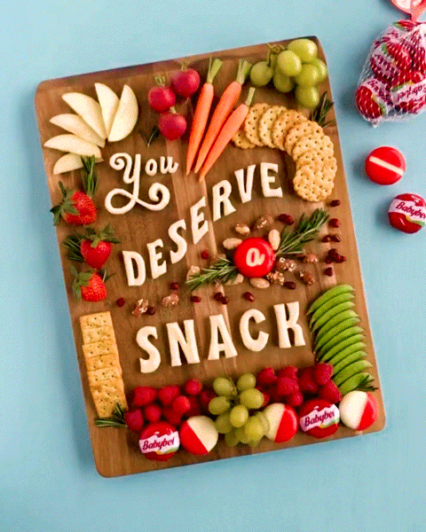 Lauren sneaking a bite of Babybel cheese from the "You Deserve a Snack" charcuterie layout made from Babybel Cheese, crackers, fruit, vegetables, nuts, and herbs.