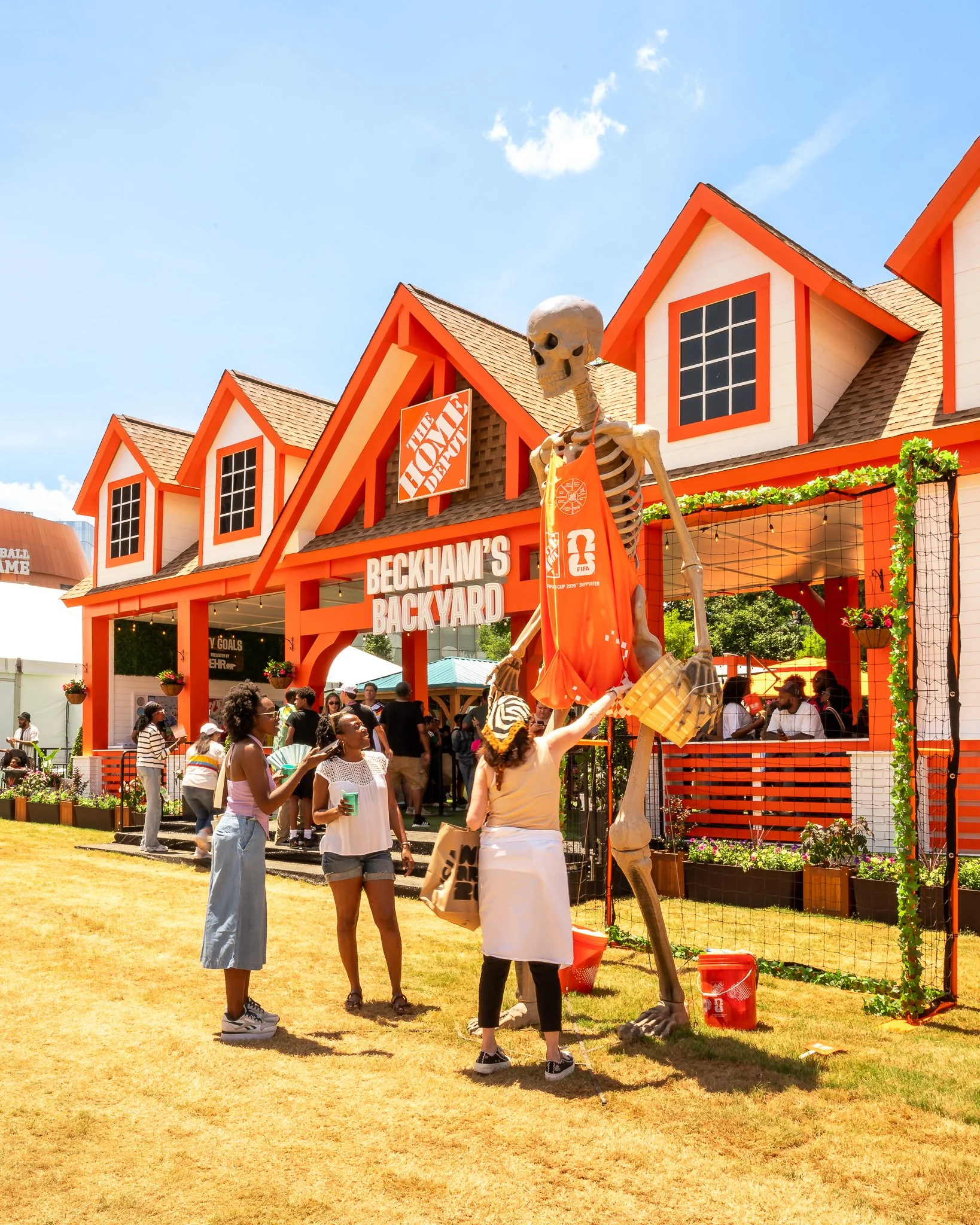 Guests relax in Beckham's Backyard at the Home Depot activation during FIFA Fan Fest Atlanta while others explore a giant skeleton holding a basket, showcasing an interactive brand activation and fan experience.