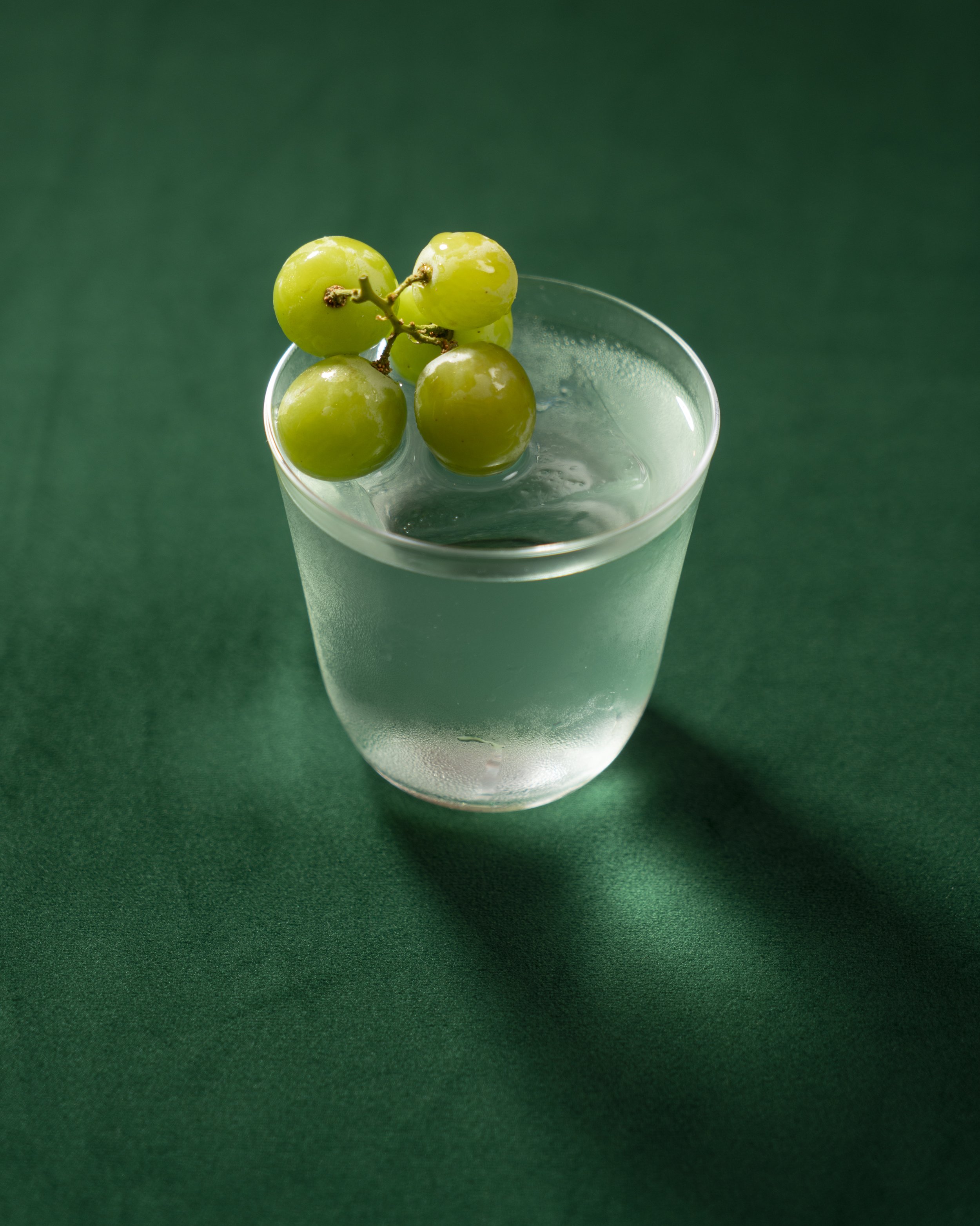 Green grapes on top of a glass of water on a green surface.