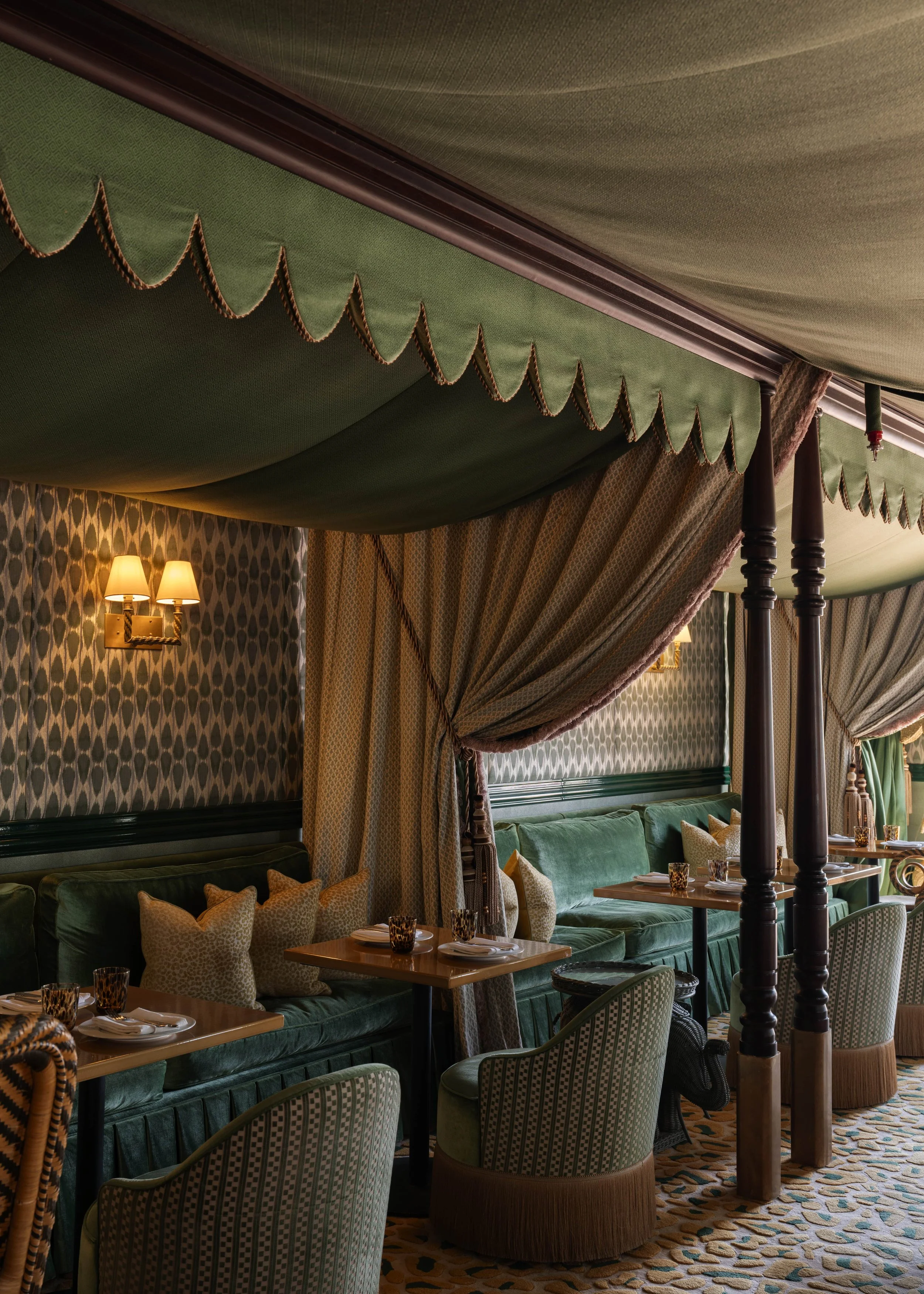 Interior view of a luxurious restaurant with green velvet booths, patterned curtains, ornate lamps, and a patterned carpet.