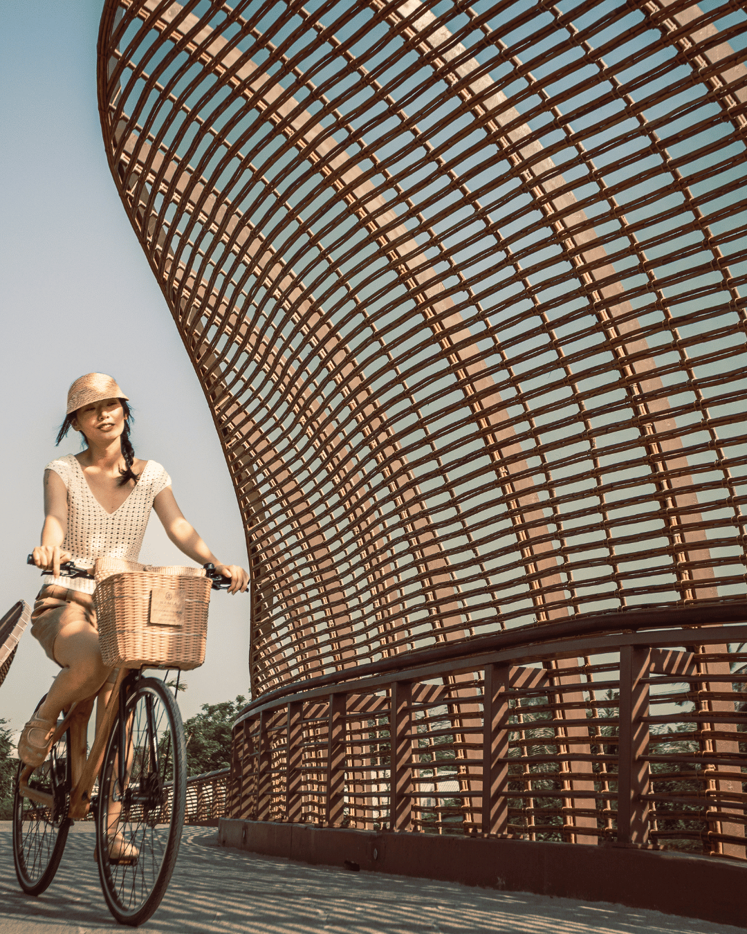 A woman riding a bicycle on a bridge with a geometric, lattice-like metal structure. | Awakened Soul - Jessika Harrison 