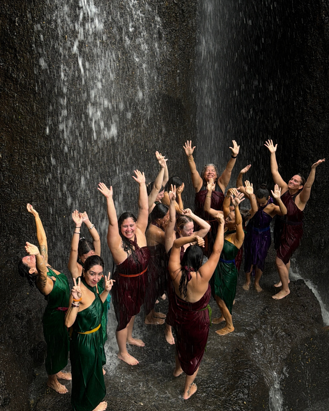 A group of women in colorful dresses dancing and enjoying under a waterfall.