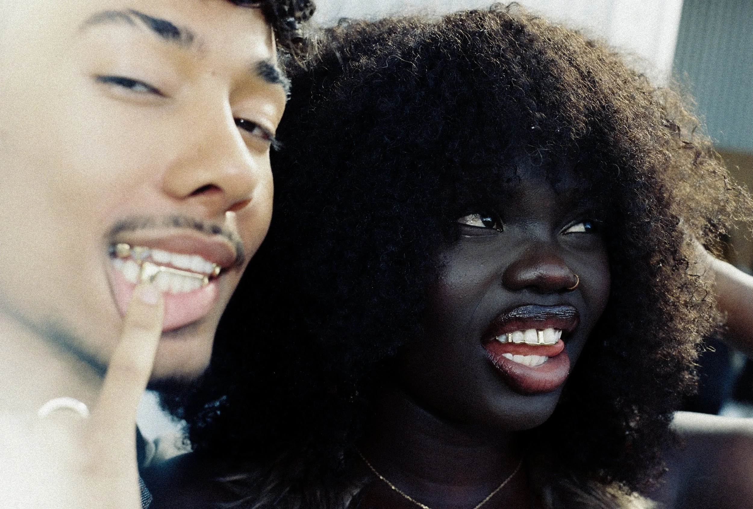 Two people smiling, one with finger pointing at a gold tooth.