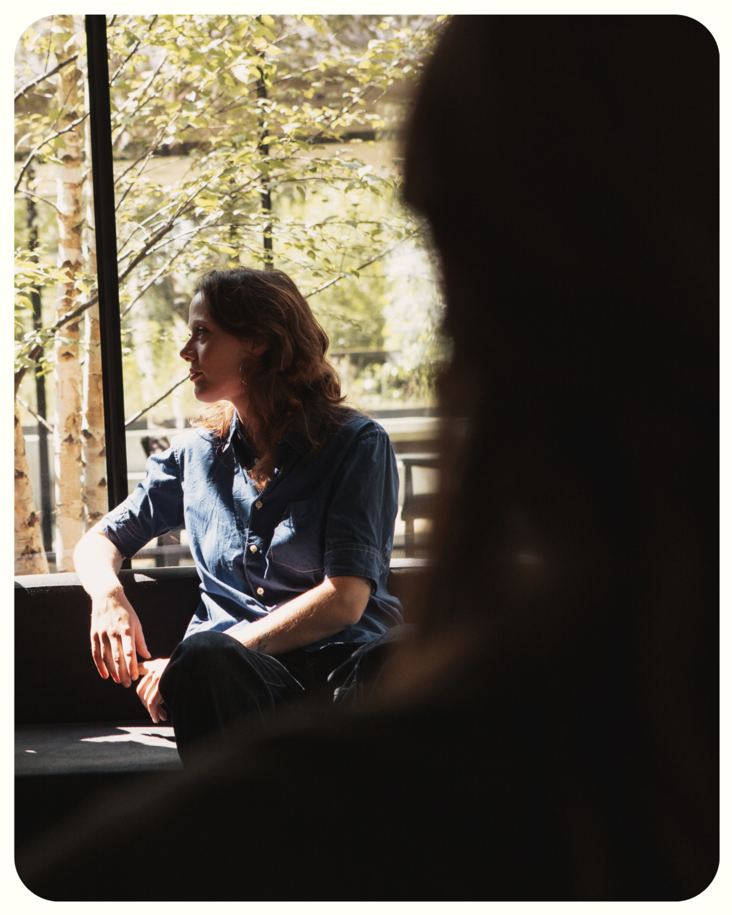 A Woman in front of a window sitting on a couch thinking about her coaching and listening to her coach