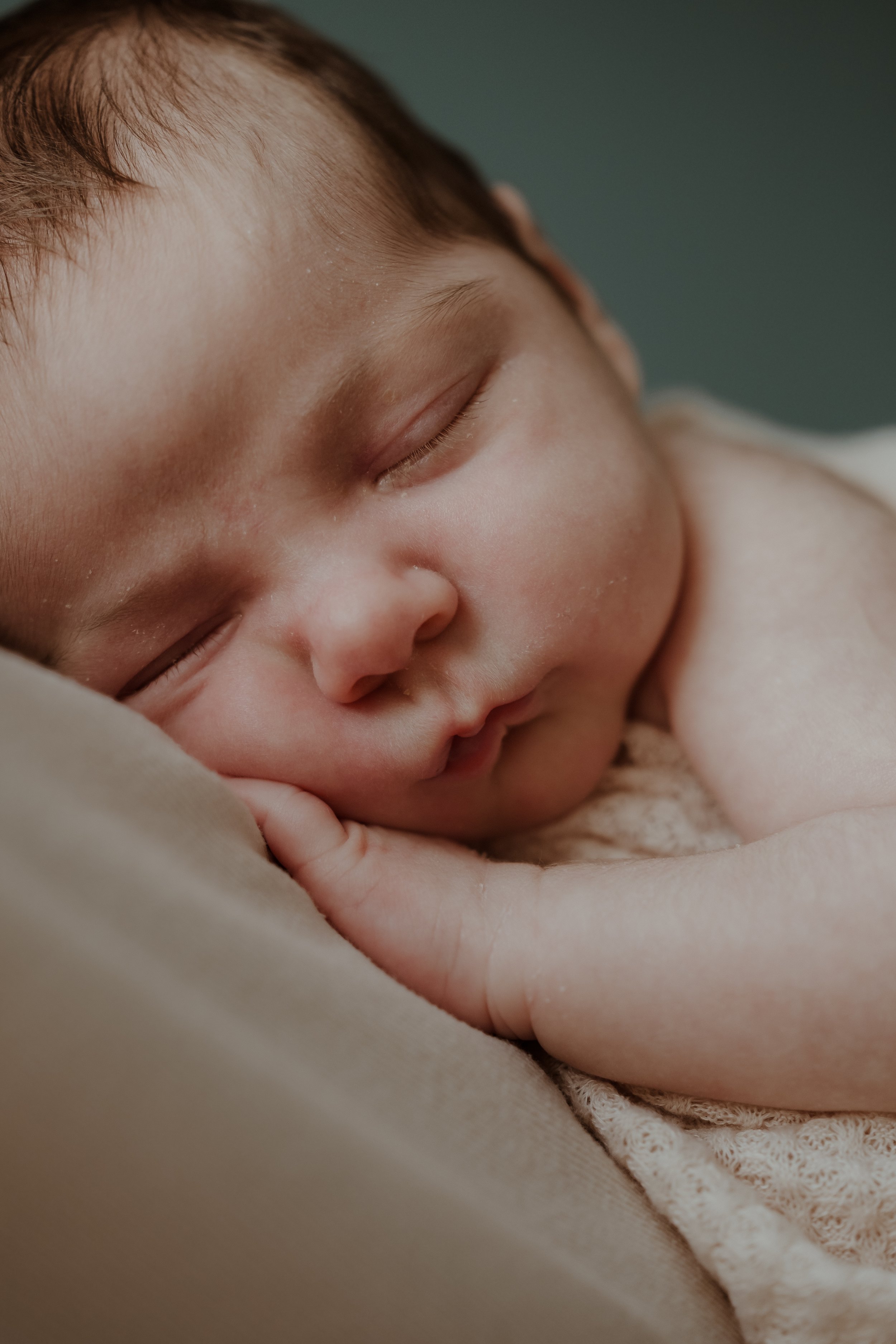 A close-up of a sleeping baby with closed eyes, resting peacefully with hand near face, soft lighting, and neutral background.