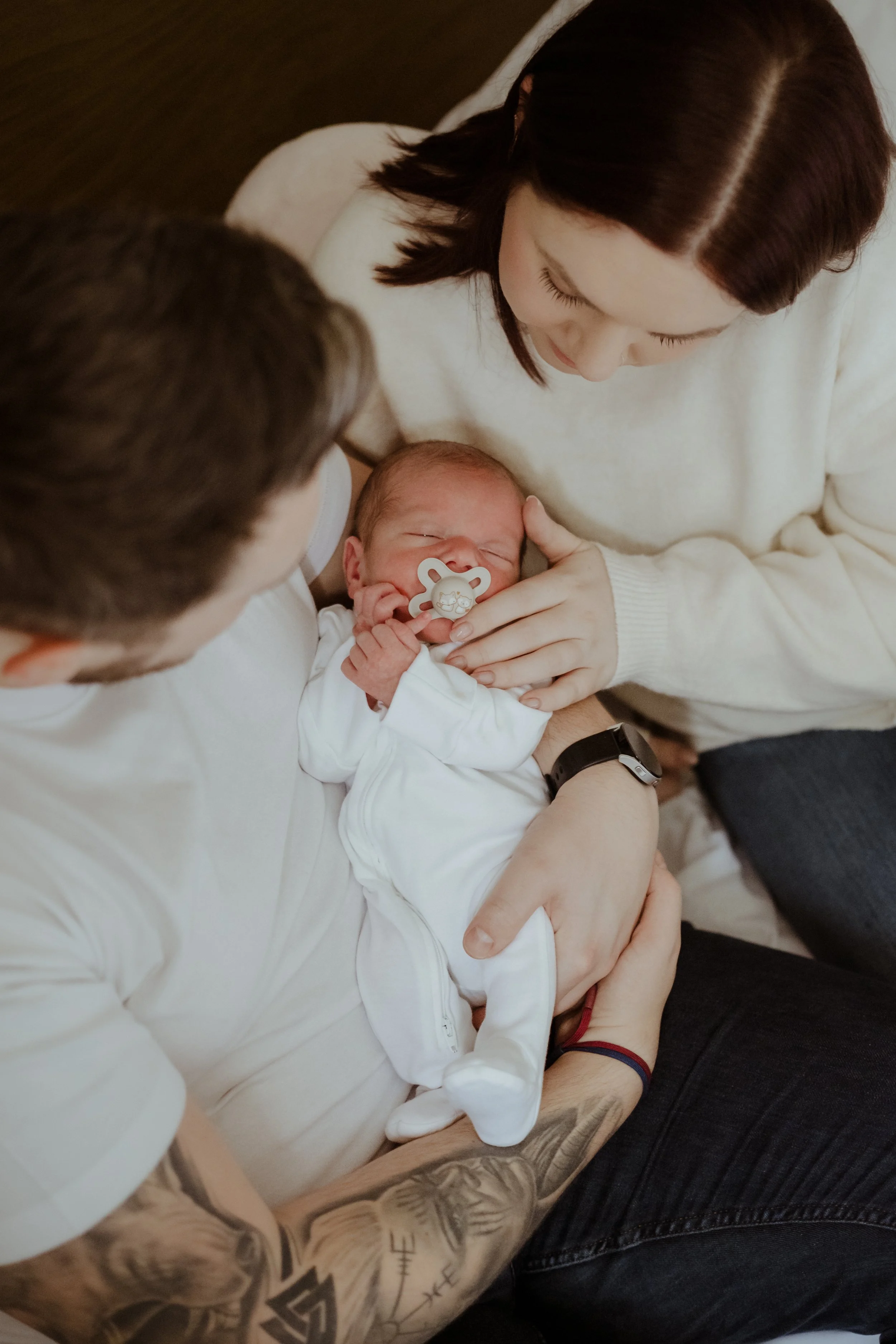 A person with tattoos holding a newborn baby with an adult woman looking at the baby
