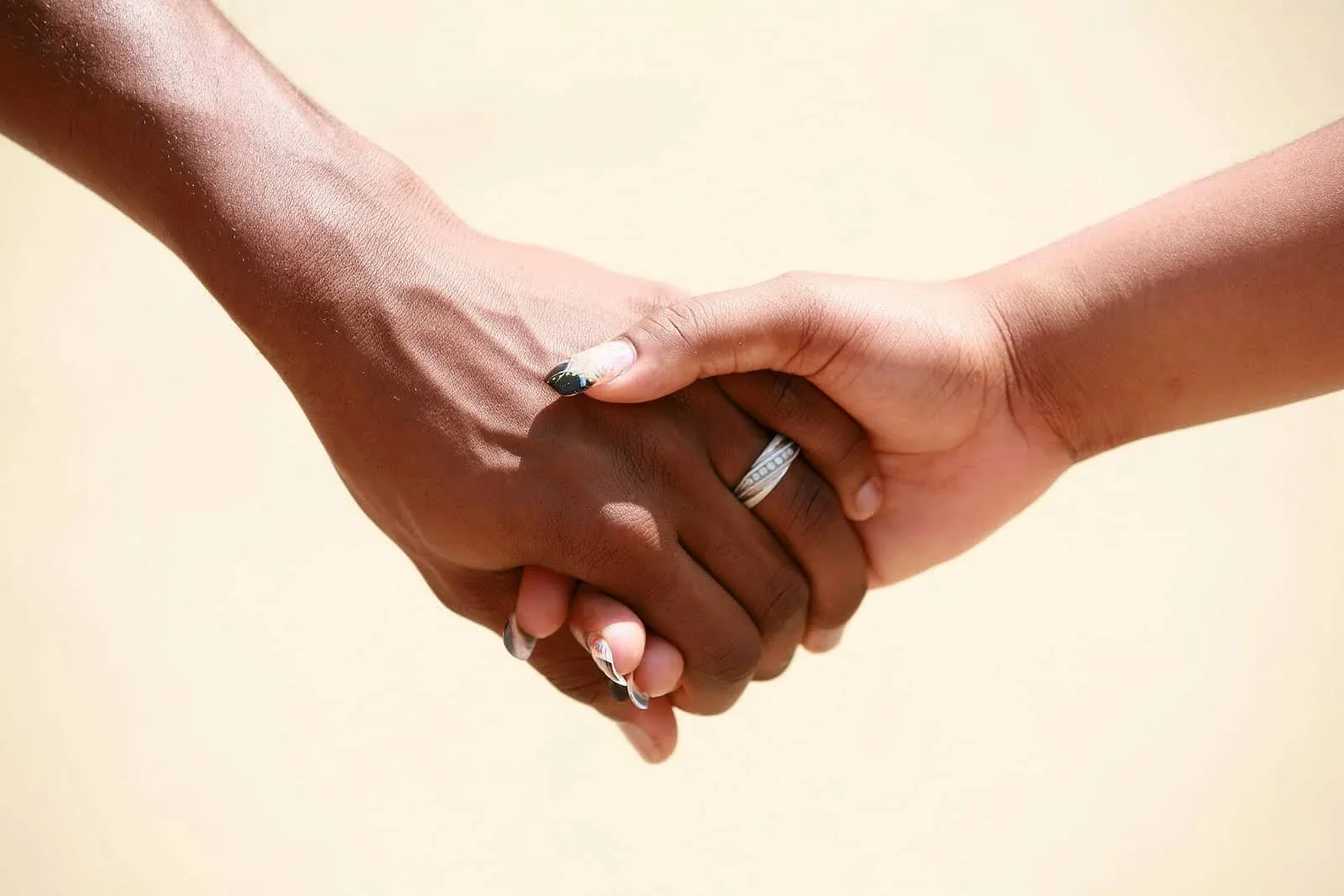 A close-up of two people holding hands, one wearing a silver ring. The background is blurred, emphasizing their intertwined fingers as a gesture of connection and support. Learn how therapy for intimacy issues in Walnut Creek, CA