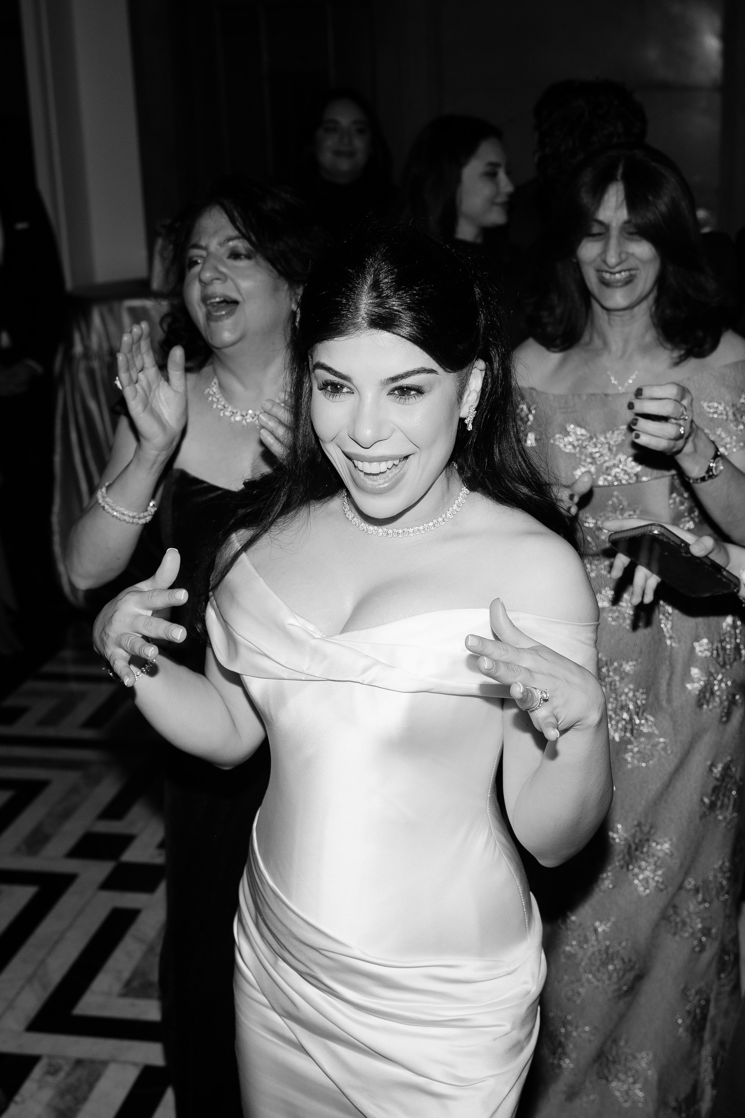 Jihan dancing and laughing with guests at the reception, in black and white
