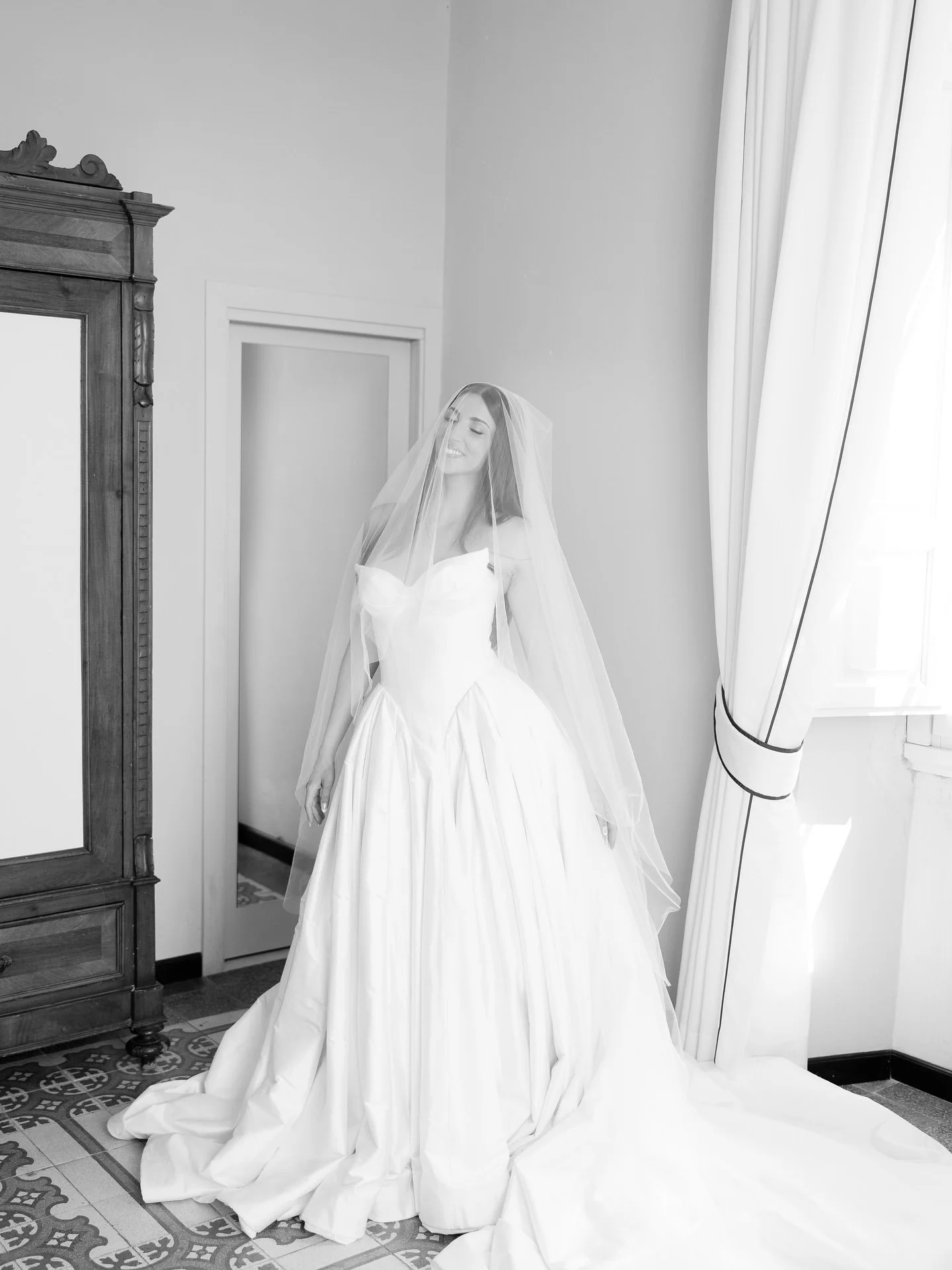Black and white portrait of bride Marilena in her Leah Da Gloria gown and veil beside an antique wardrobe at Villa Belvedere