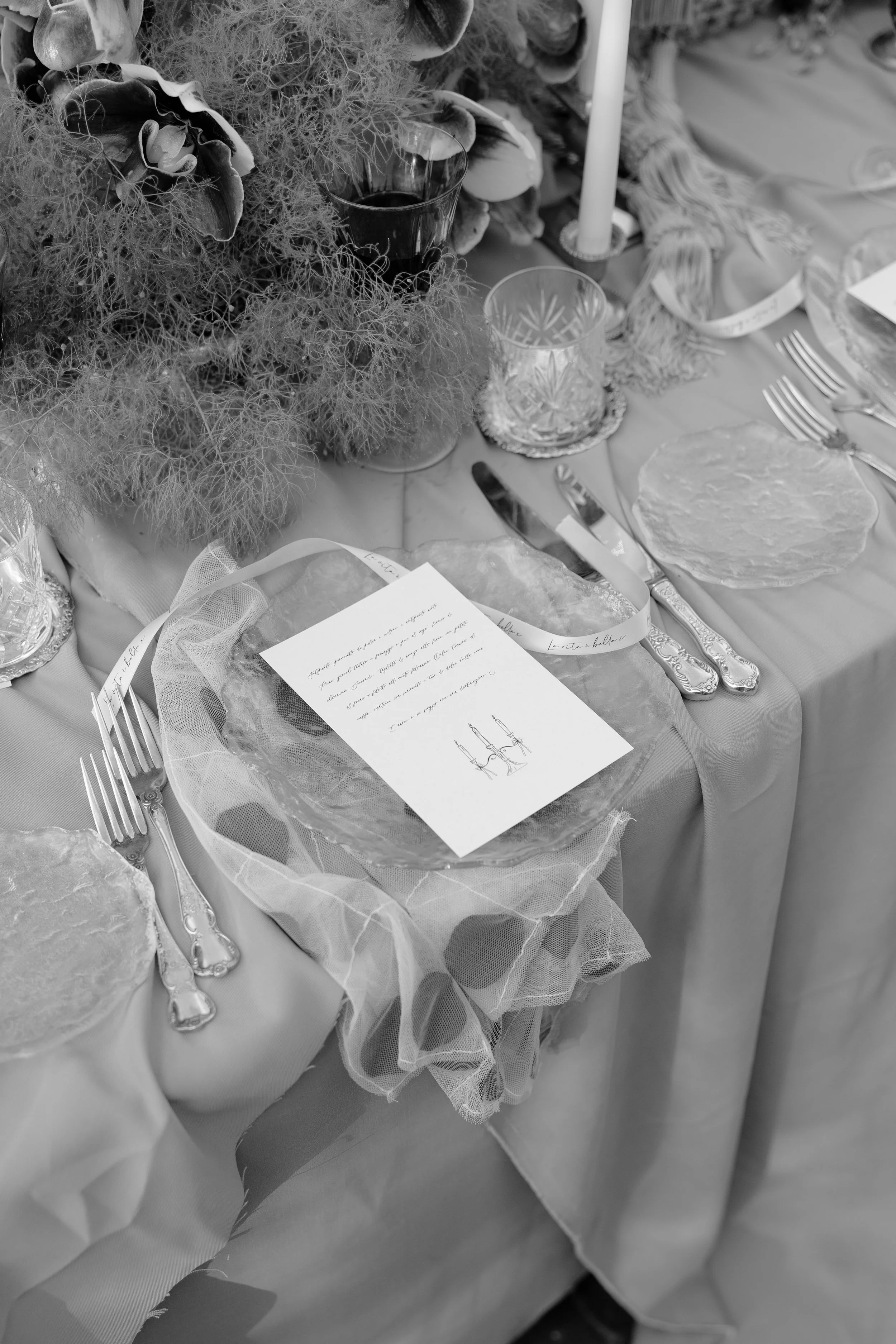 A decorated table set for a formal occasion with cutlery, glassware, a candle, a menu card, and a floral centerpiece.