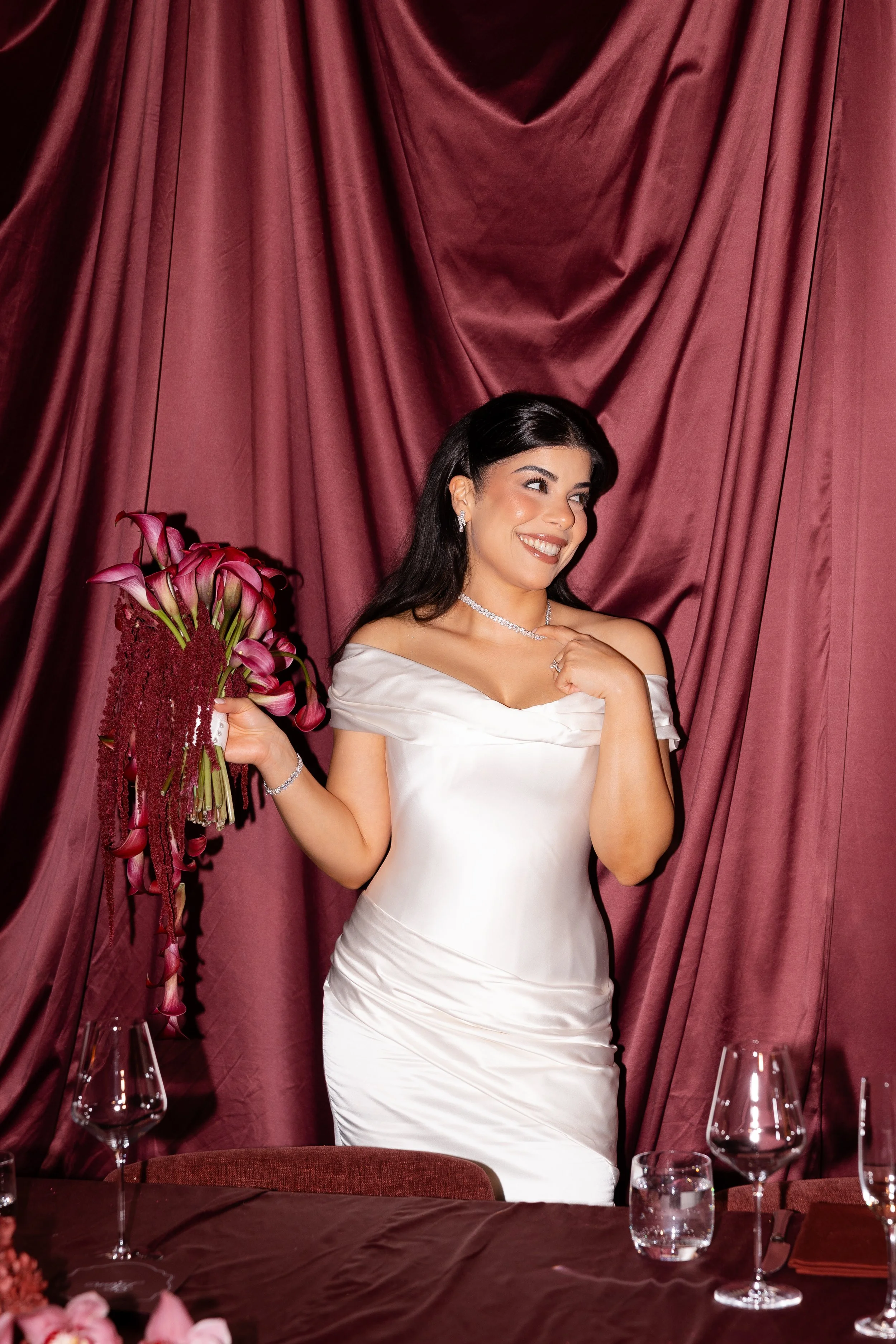 Jihan smiling in front of burgundy silk drapes holding a burgundy bouquet