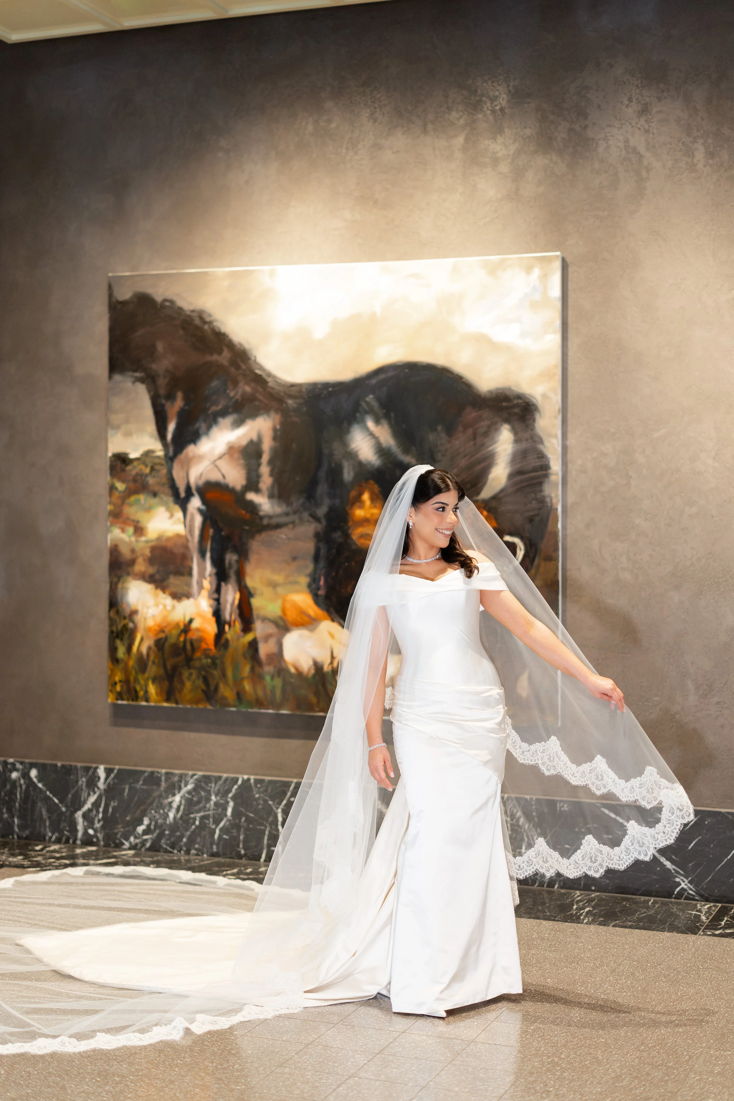 Jihan in a long lace-edged veil beside a framed artwork in the hotel