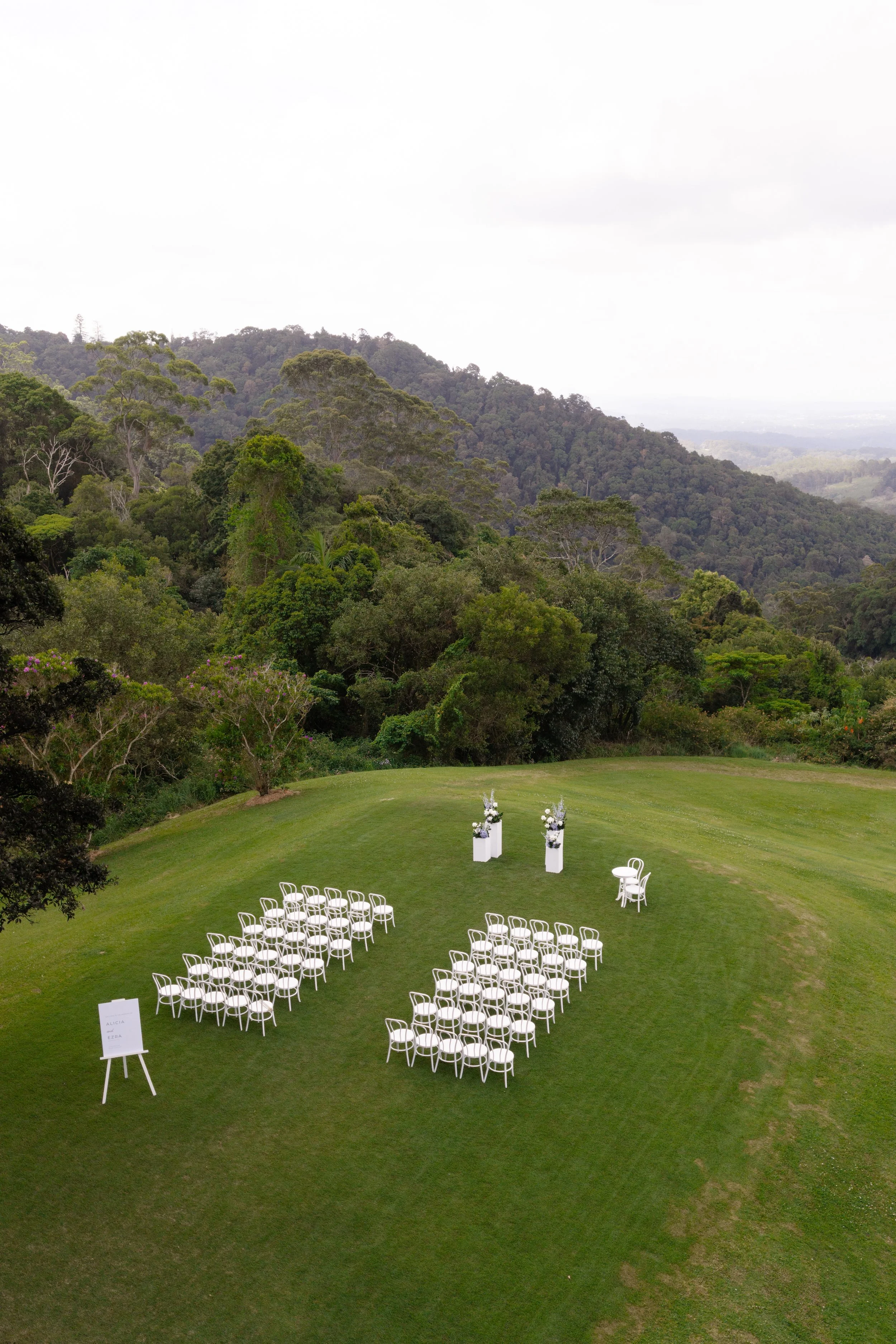 Alicia and Ezra's ceremony setup: rows of white chairs on the lawn with forested hills beyond